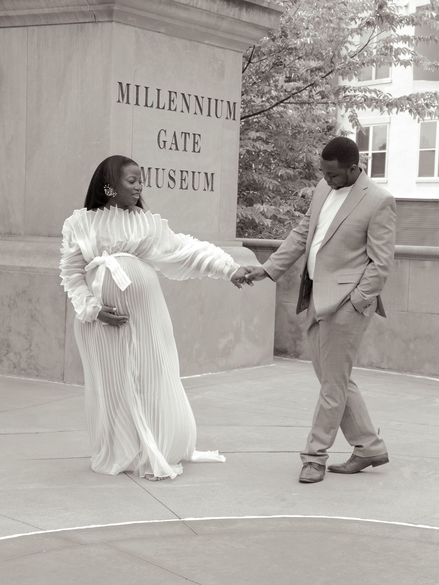 A couple holds hands outside the Millennium Gate Museum in elegant white and beige attire.