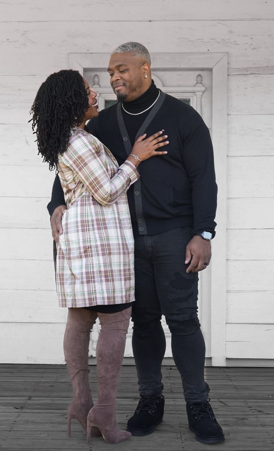A parent and child share a tender moment in matching black and plaid outfits against a white garage door background.