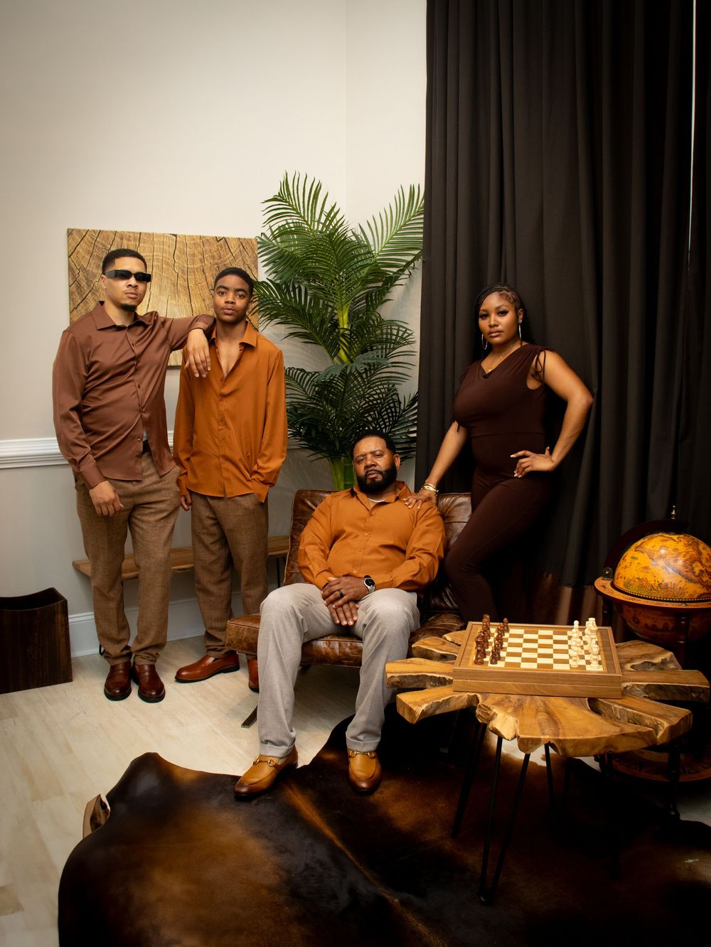 A event family photo  in brown and orange toned outfits poses in a modern interior setting with chess set and globe decorations.
