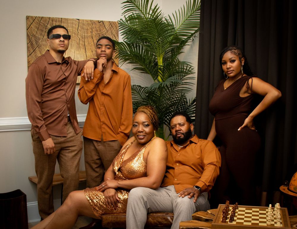 A event family photo  in brown and orange toned outfits poses in a modern interior setting with chess set and globe decorations.