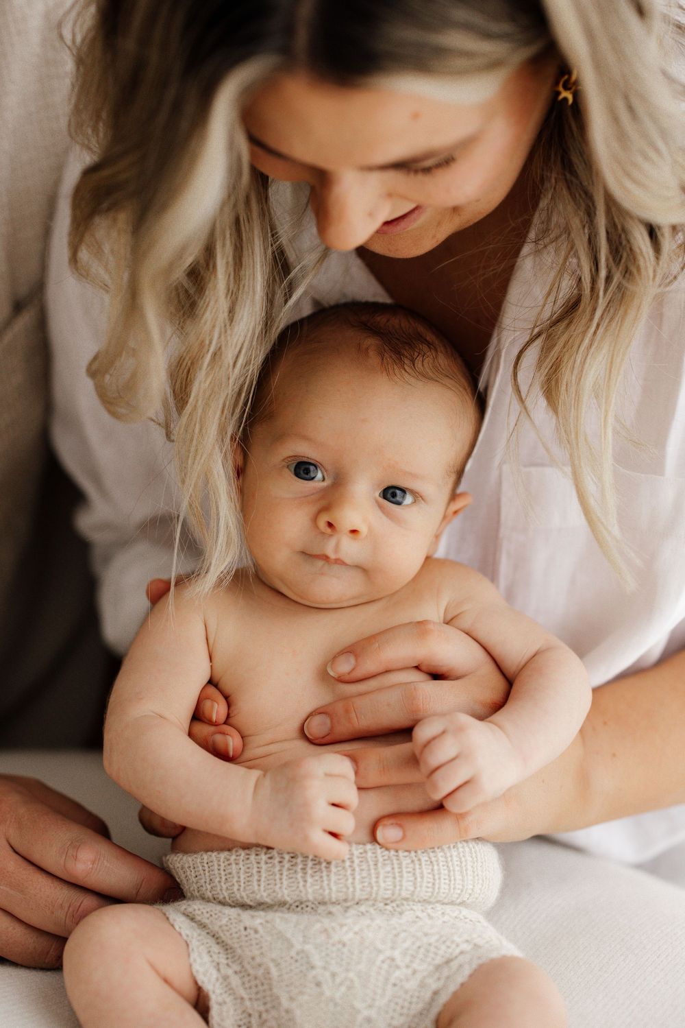 A blonde mother lovingly gazes down at her alert blue-eyed baby in a soft knit wrap.