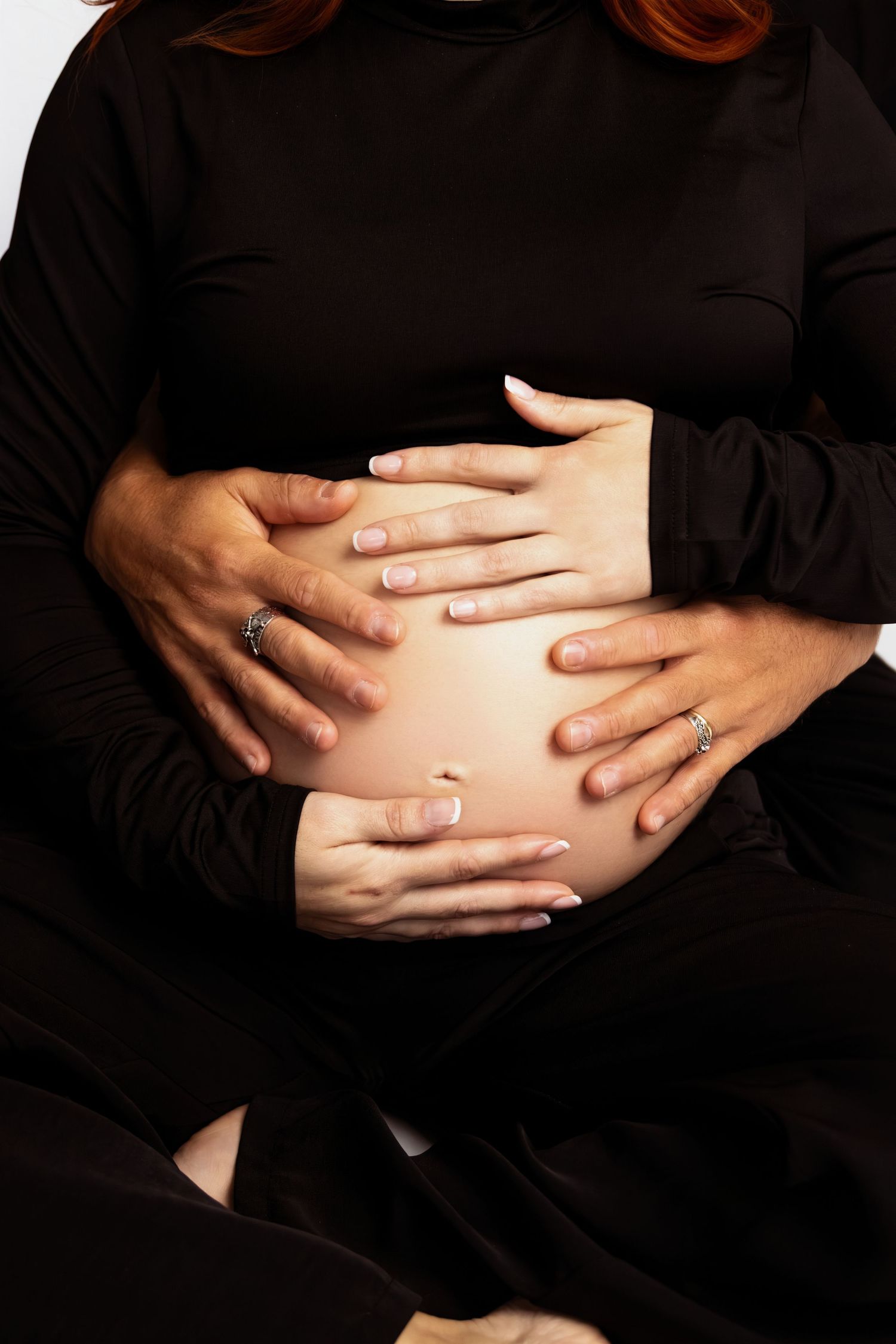 Series of hands cradling a pregnant belly against black background.