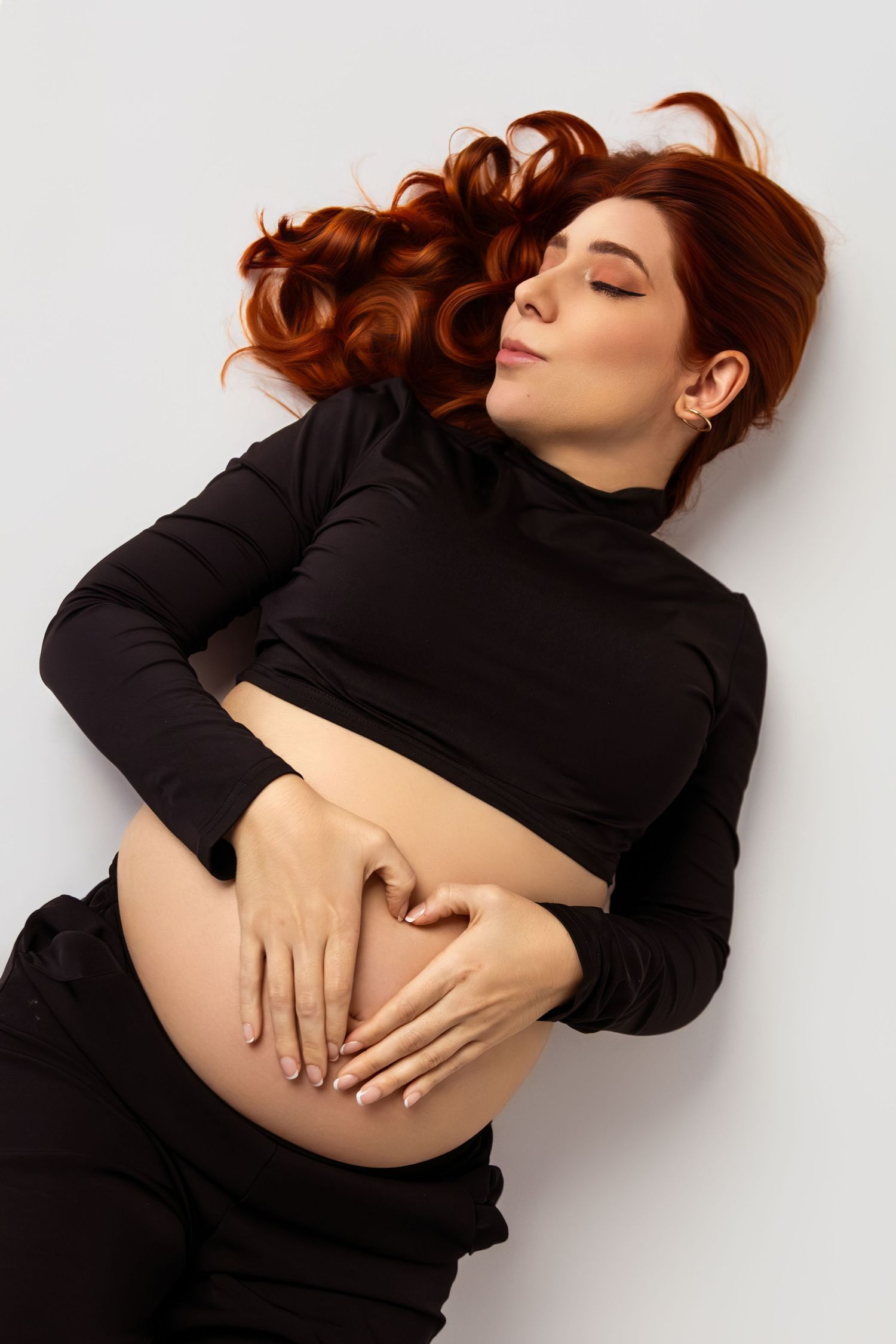 Artistic maternity photos with woman in black dress lying on white background.