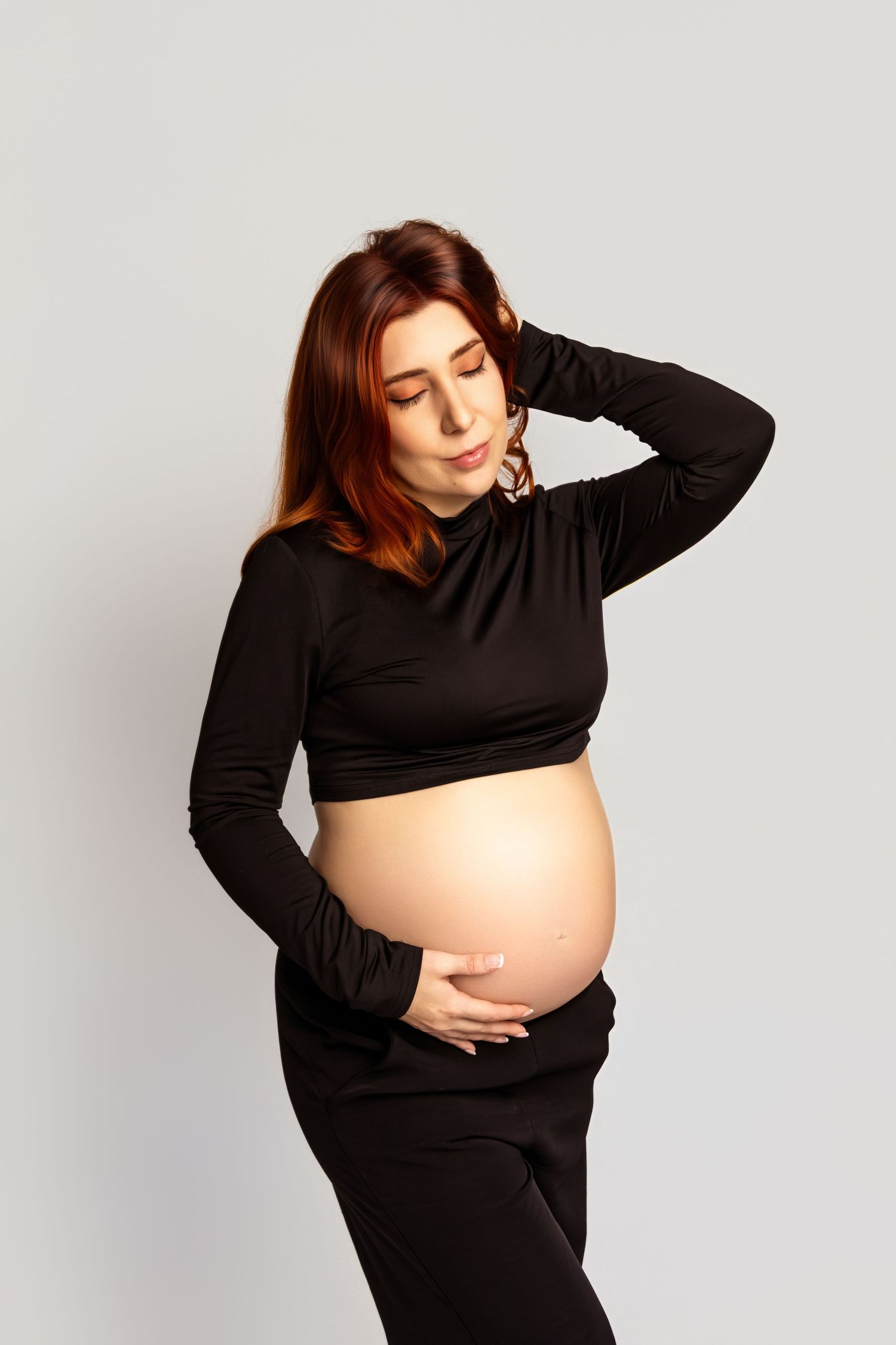 Stylish pregnancy photoshoot with woman in black crop top against white background.