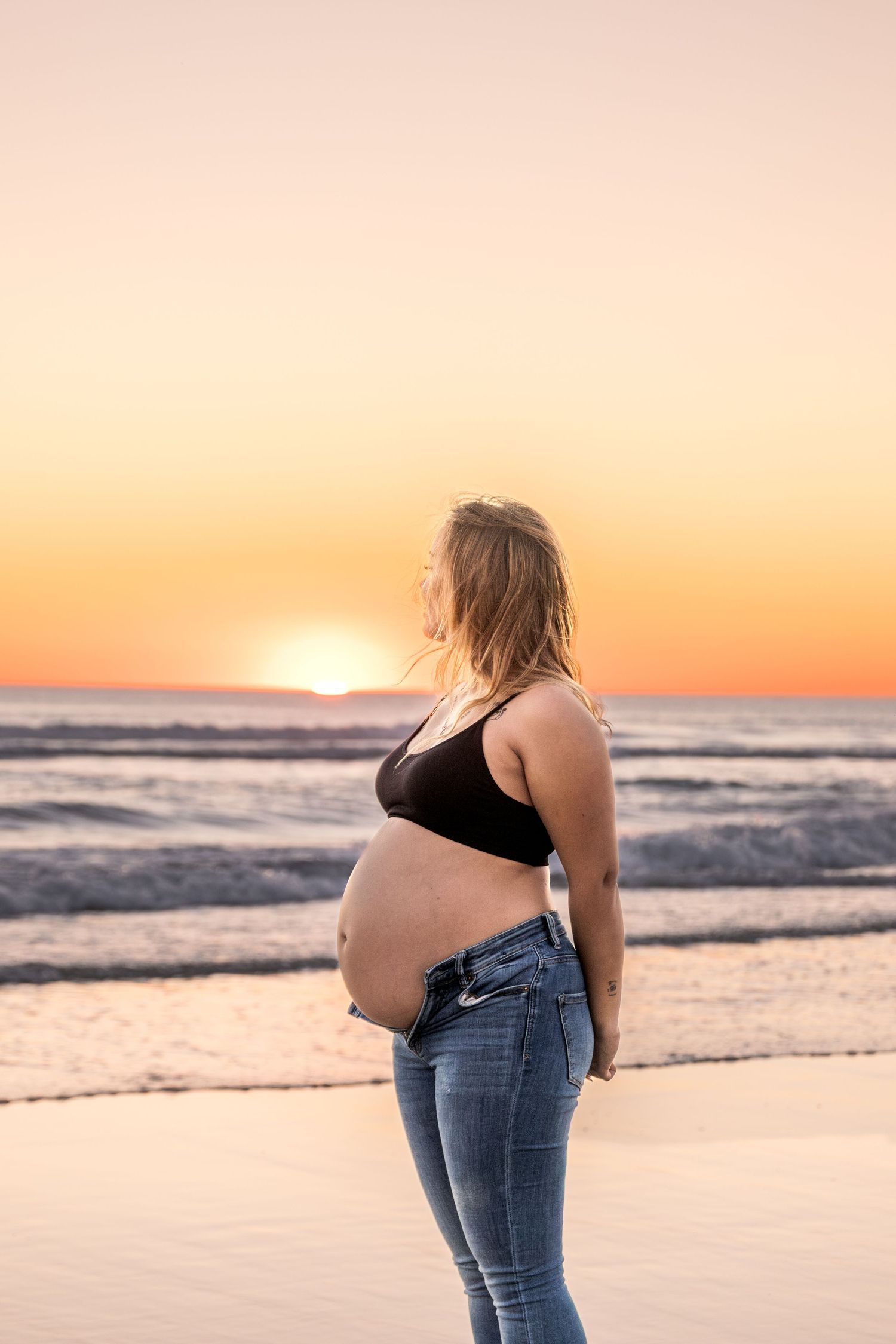 Maternity beach portraits with waves and sunset in background.