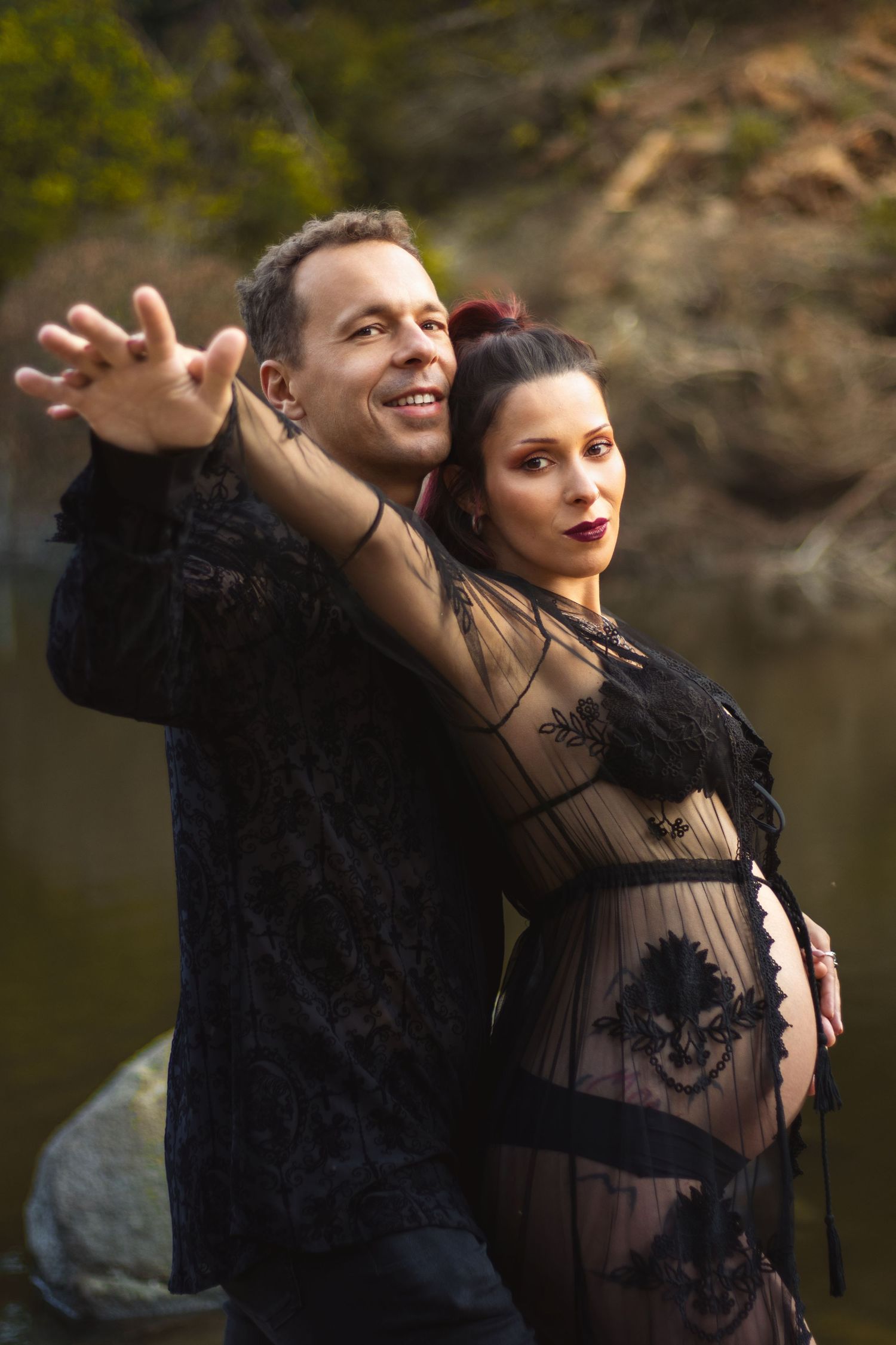 Couple in dark formal wear pose dramatically during maternity photoshoot.