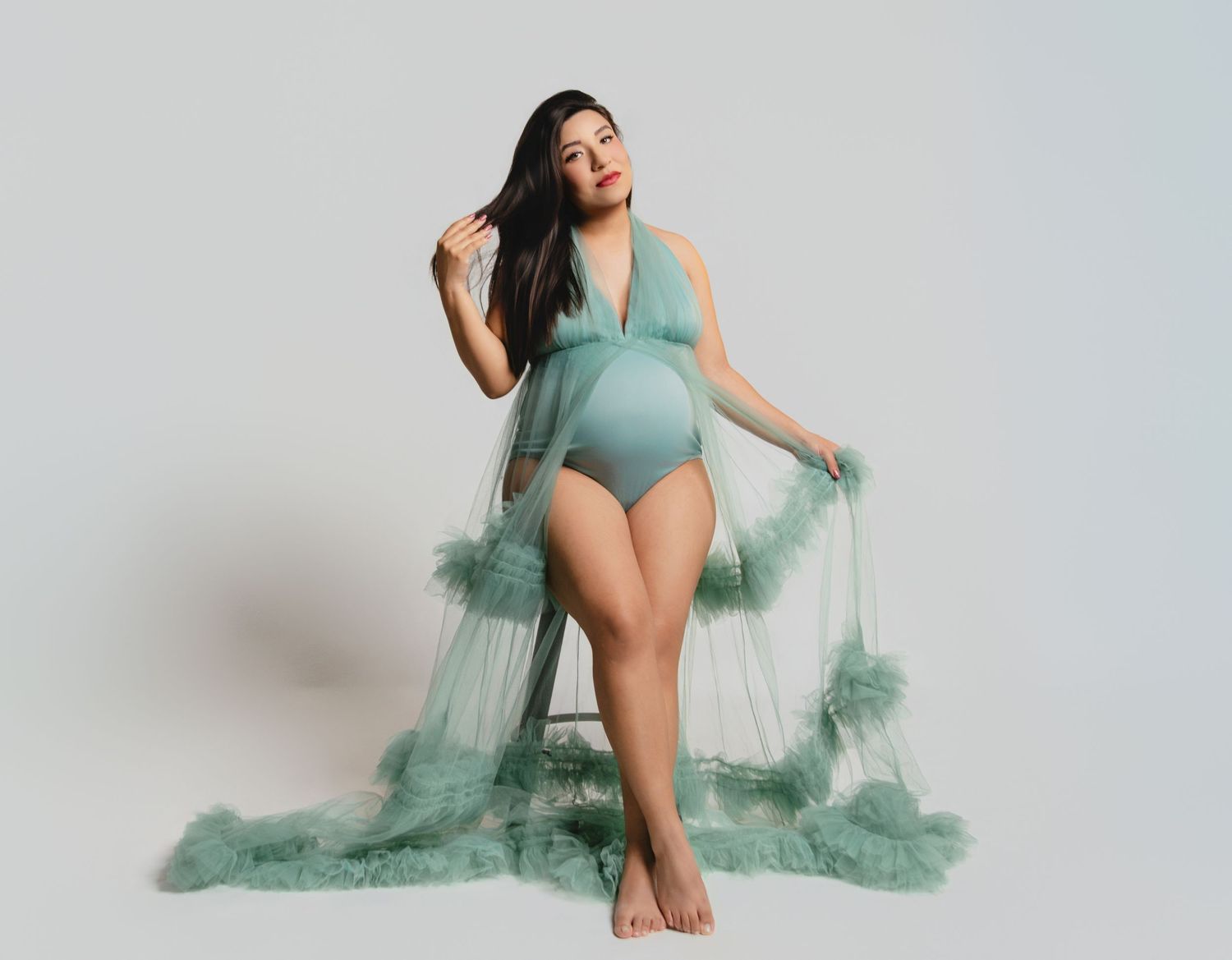 Artistic maternity photos in mint green tulle dress against light backdrop.