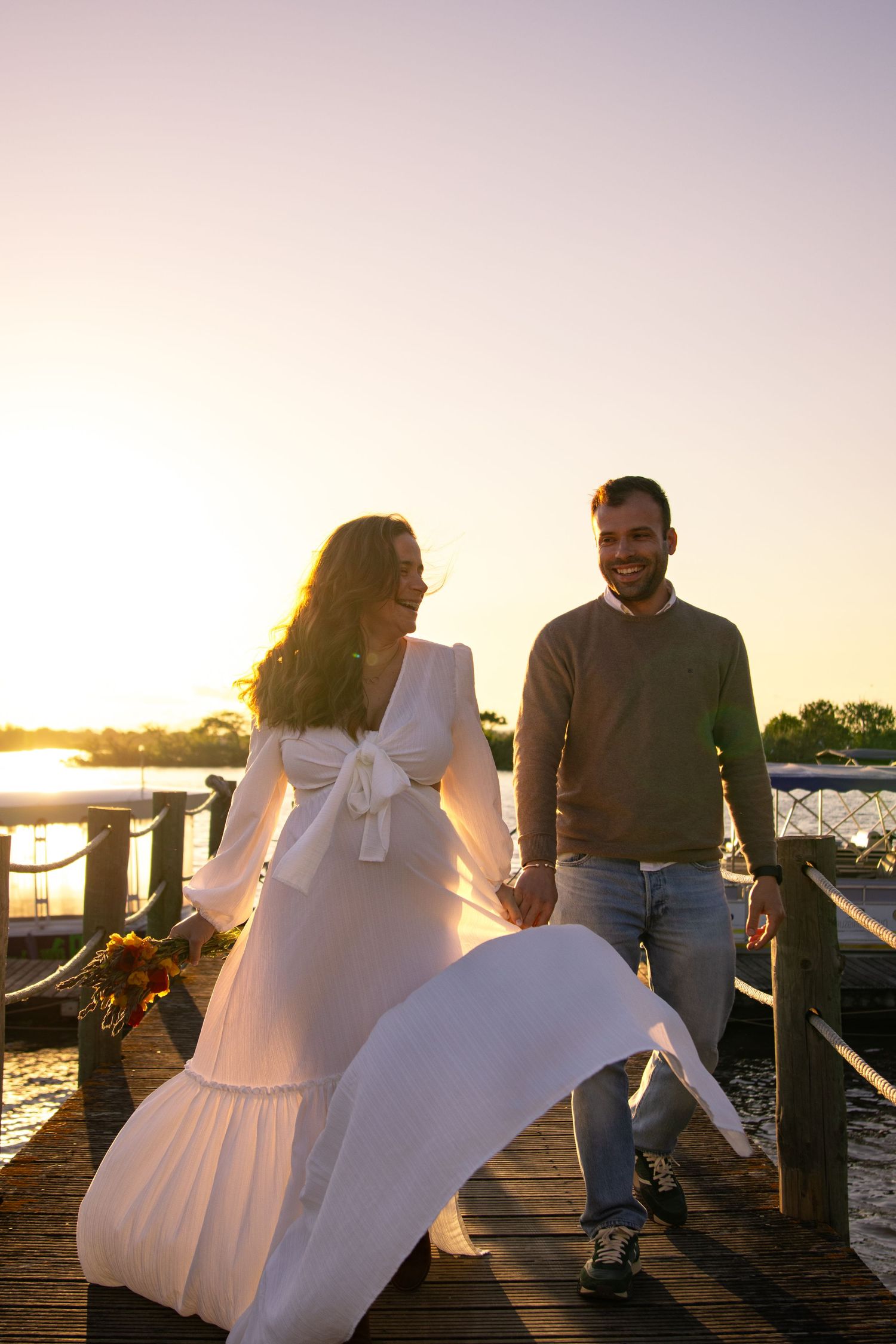 Sunset photoshoot on a wooden dock with flowing white dress against golden light.