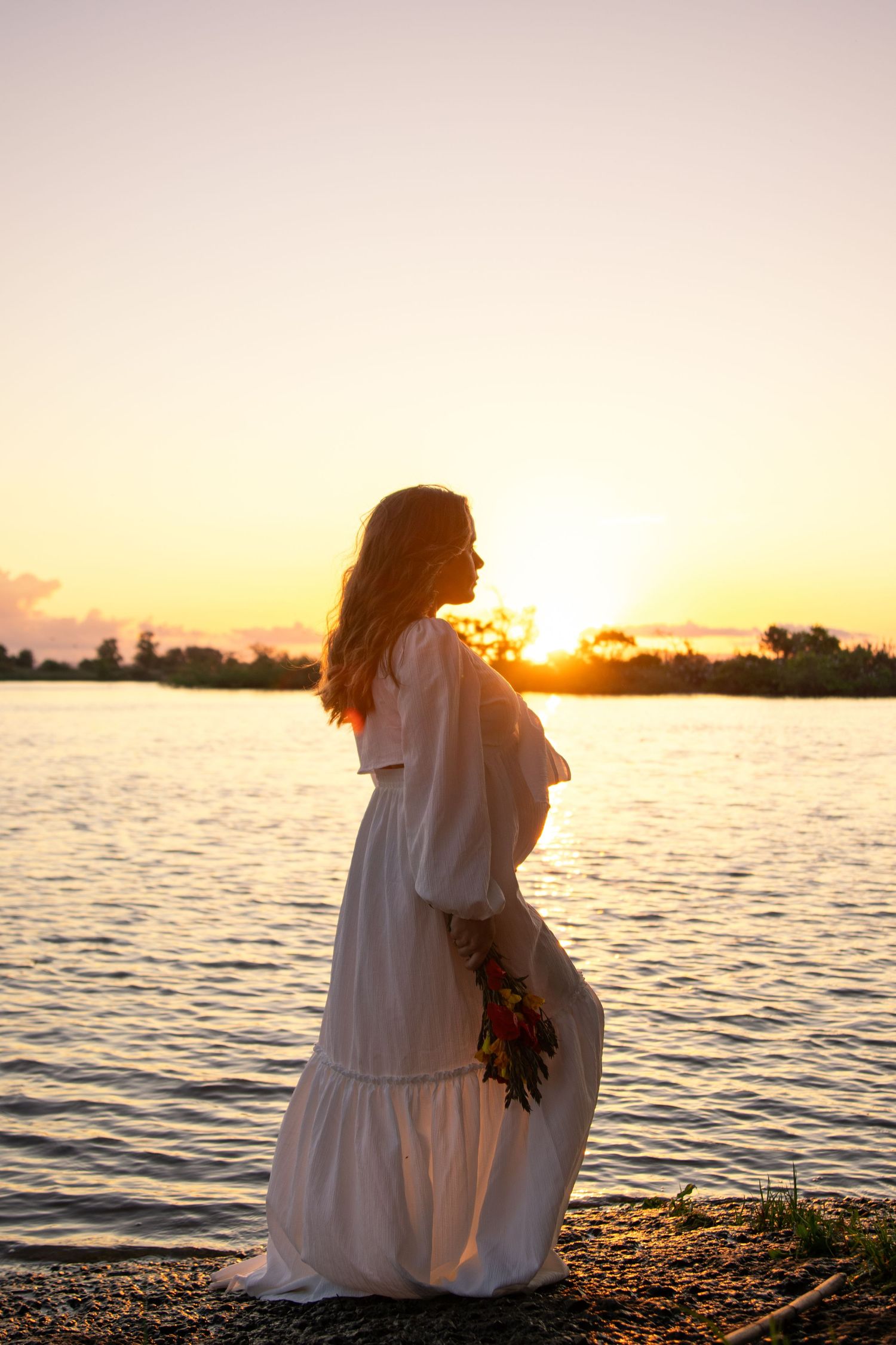 Peaceful waterfront scene at sunset with figures sitting by the shore.