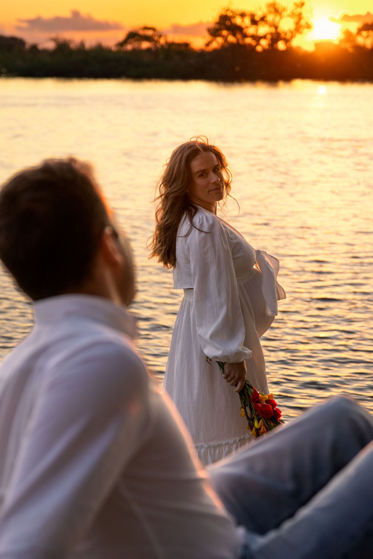 Romantic sunset photos by the water with white dress and warm golden light.