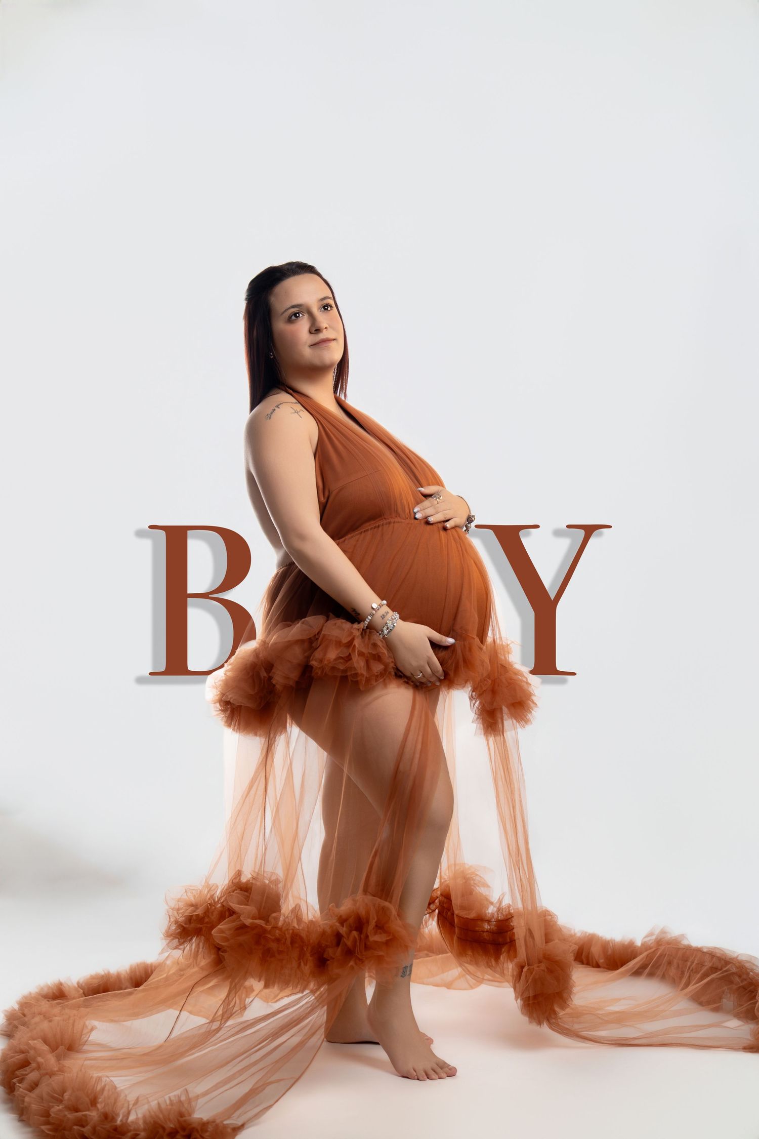 Maternity photography featuring flowing rust-colored tulle dress against white backdrop.