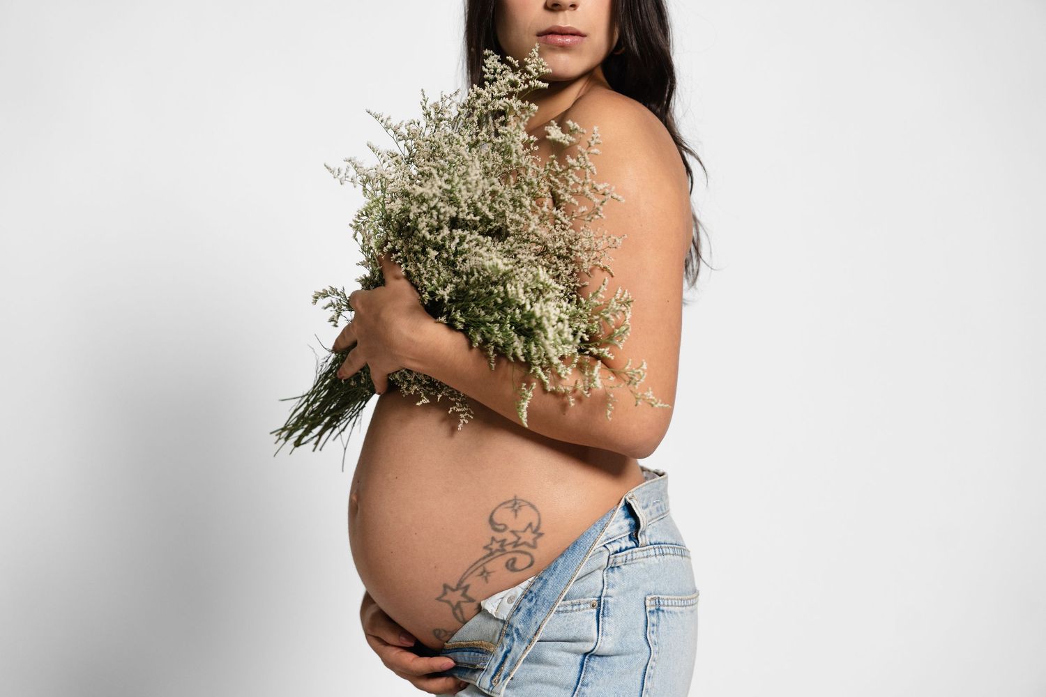 Artistic maternity photo with woman holding flowers against white background.
