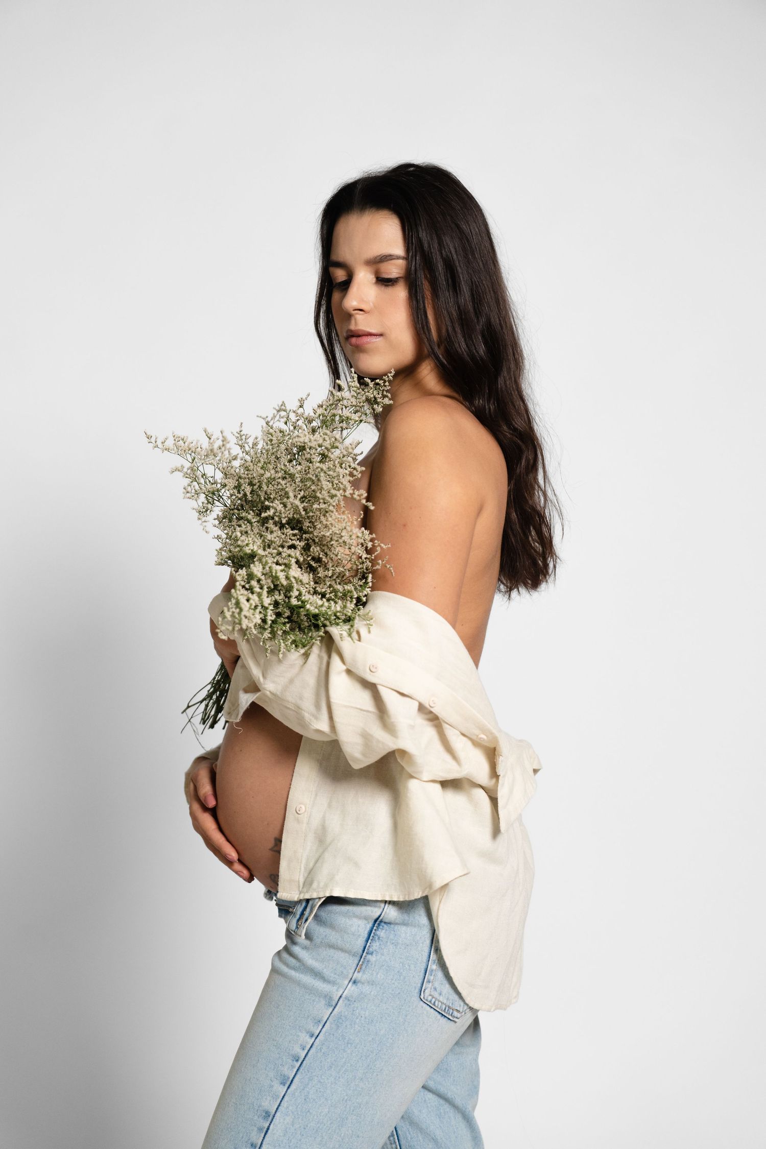 Woman in off-shoulder top holding white flowers against white backdrop.