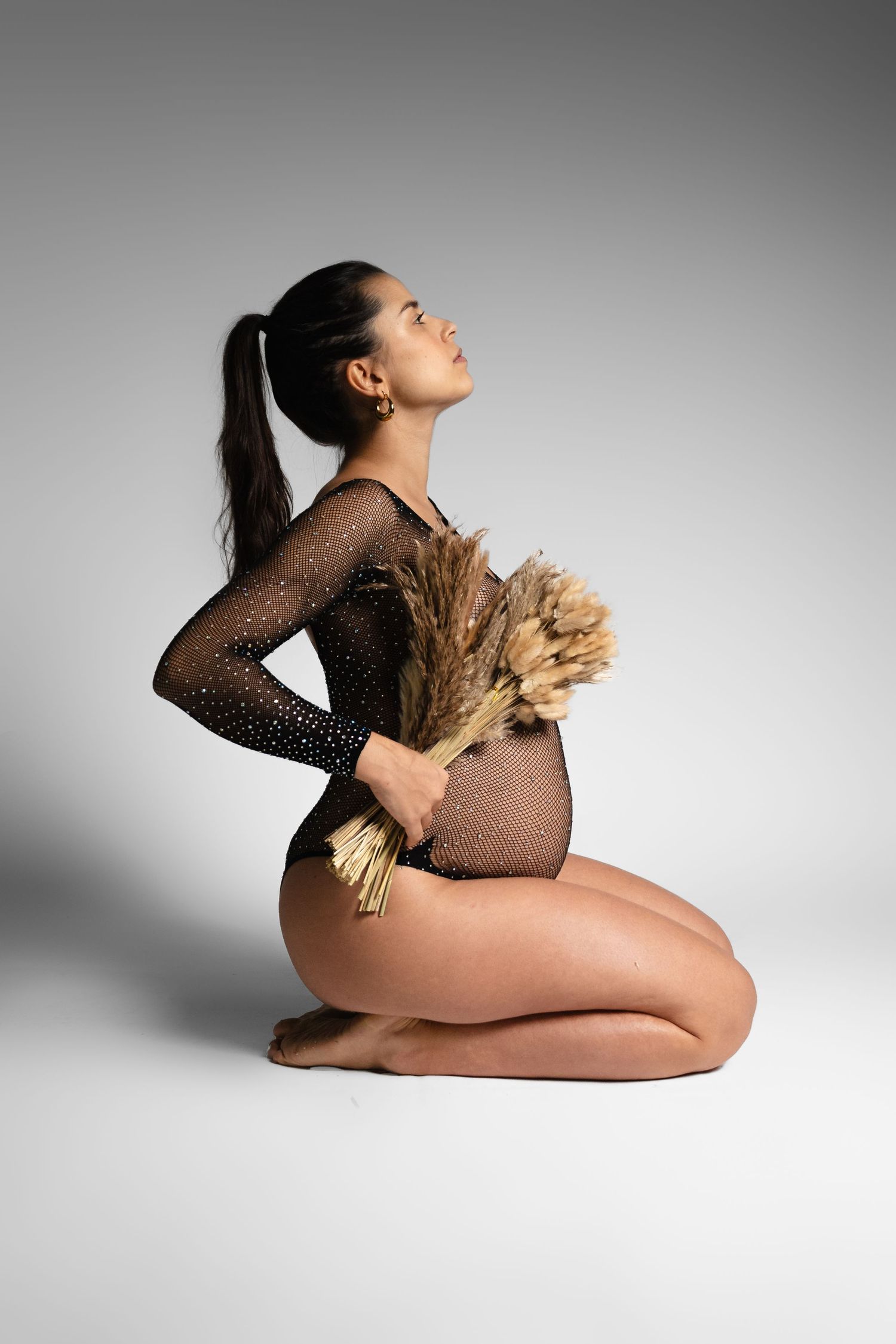 Artistic maternity photos with woman in sheer dress holding dried wheat stalks.