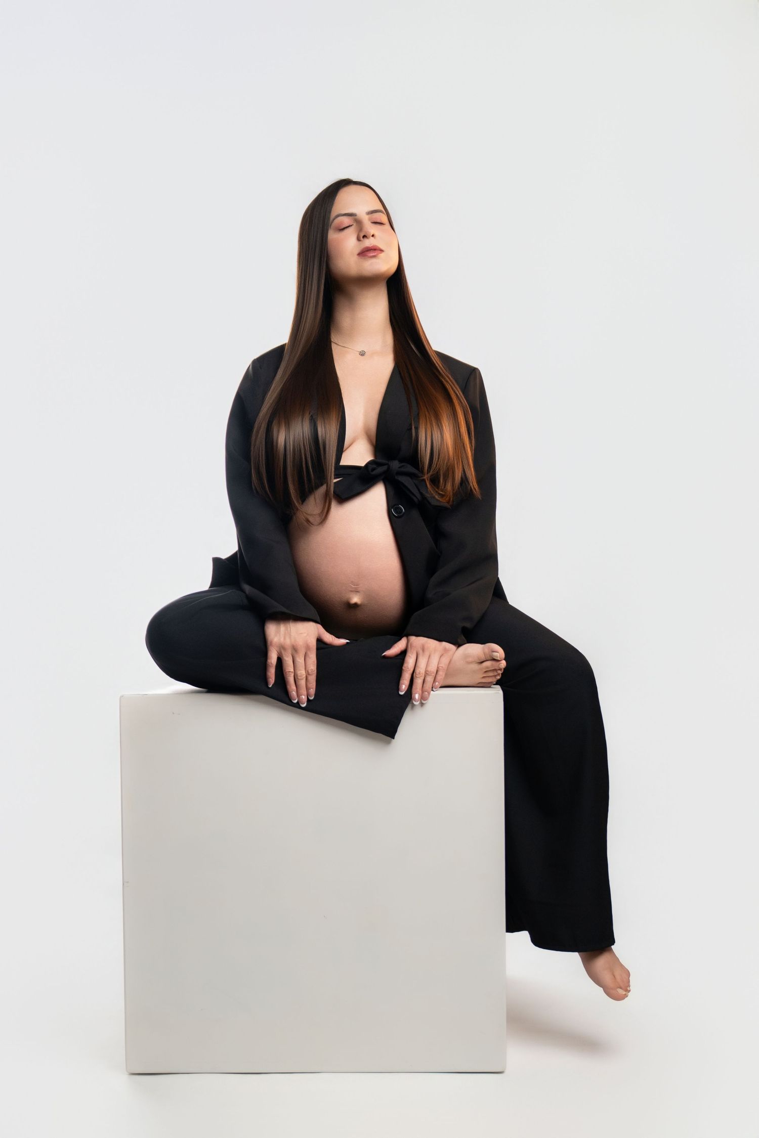 Modern maternity photos on white cube featuring black business attire.
