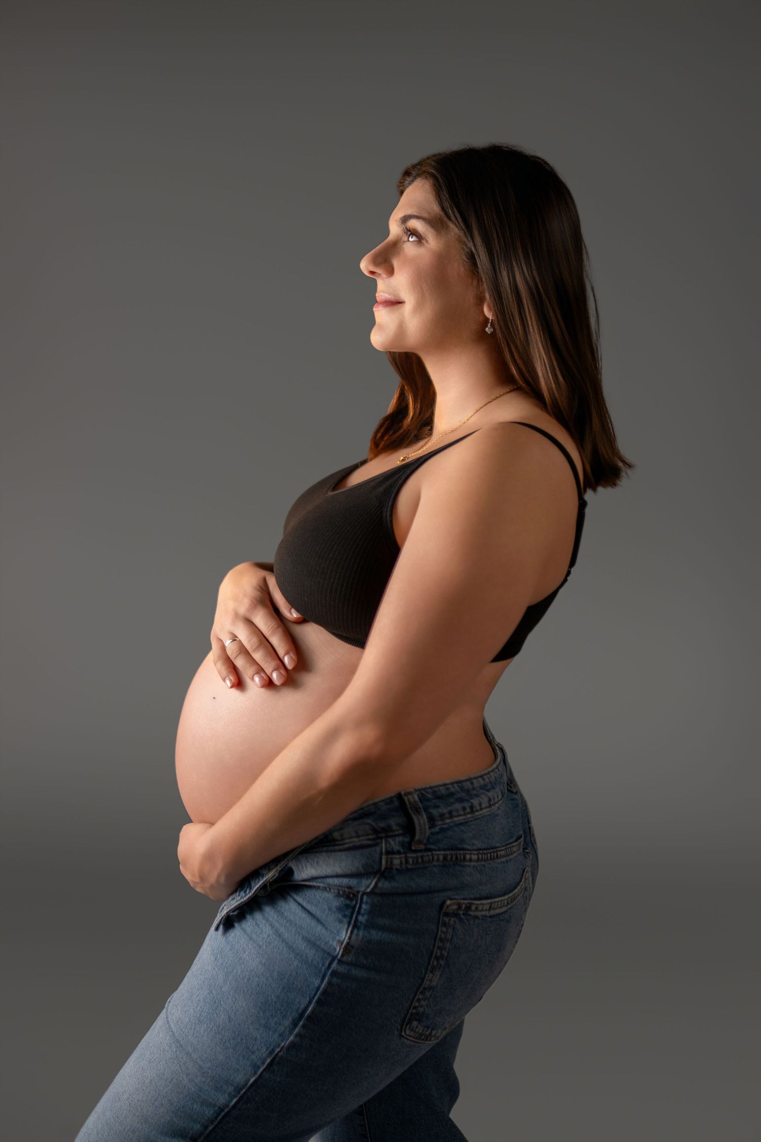 Artistic maternity portraits against grey backdrop showing silhouette of pregnant belly.