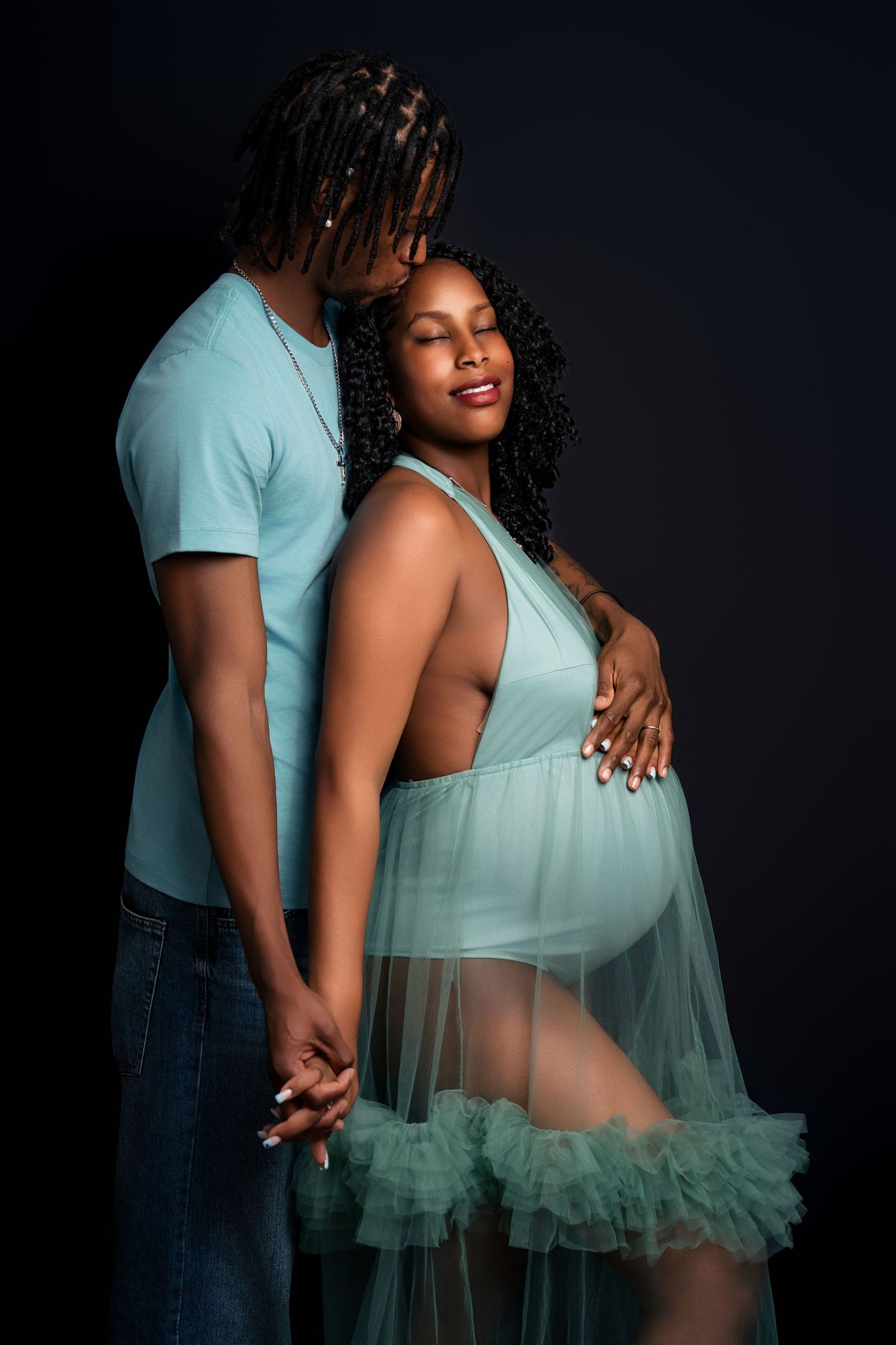 Intimate maternity portrait in mint green sheer dress against dark background.