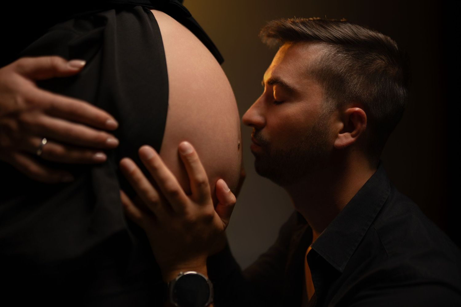 Dramatic low-key maternity photography with moody lighting and dark background.