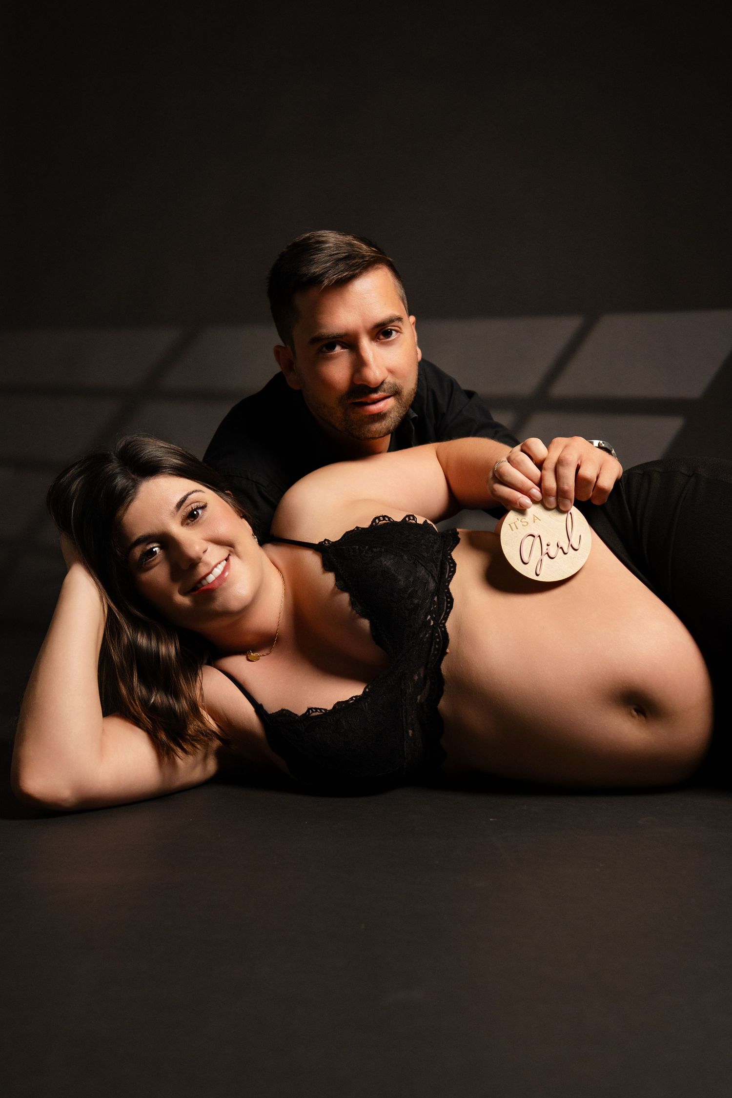 Artistic low-key maternity photography with dramatic side lighting on dark floor.