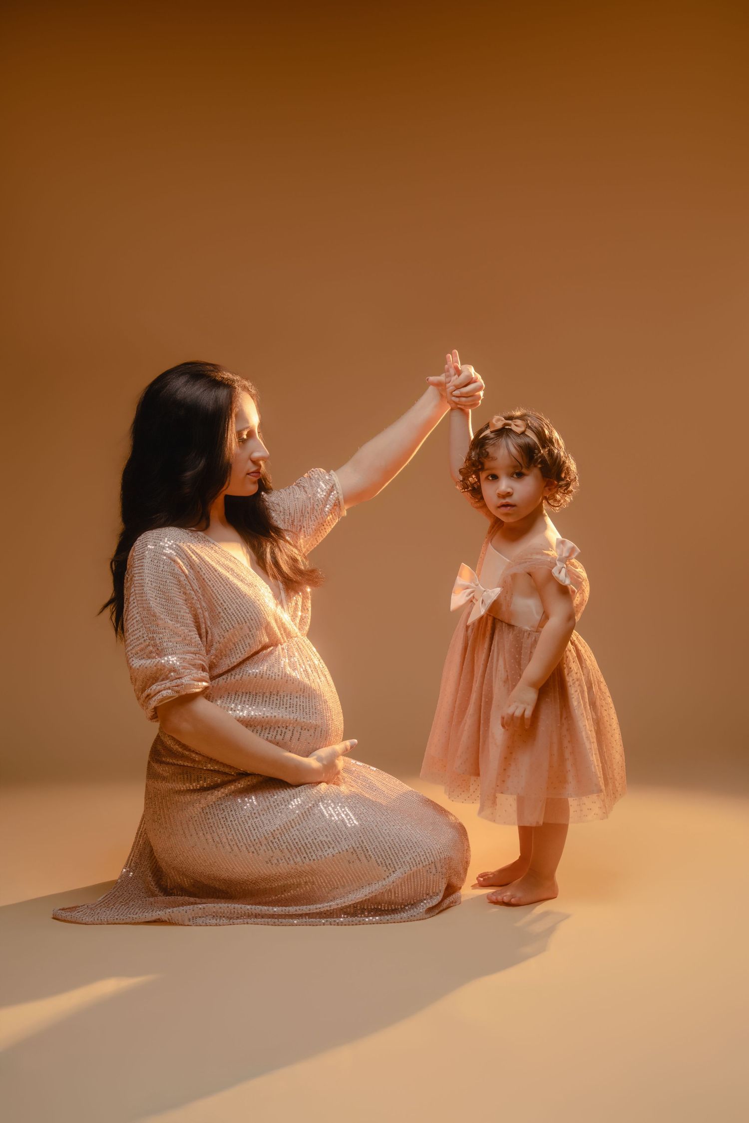 A tender moment captured in warm lighting shows a parent and child in white outfits sitting together on the floor.