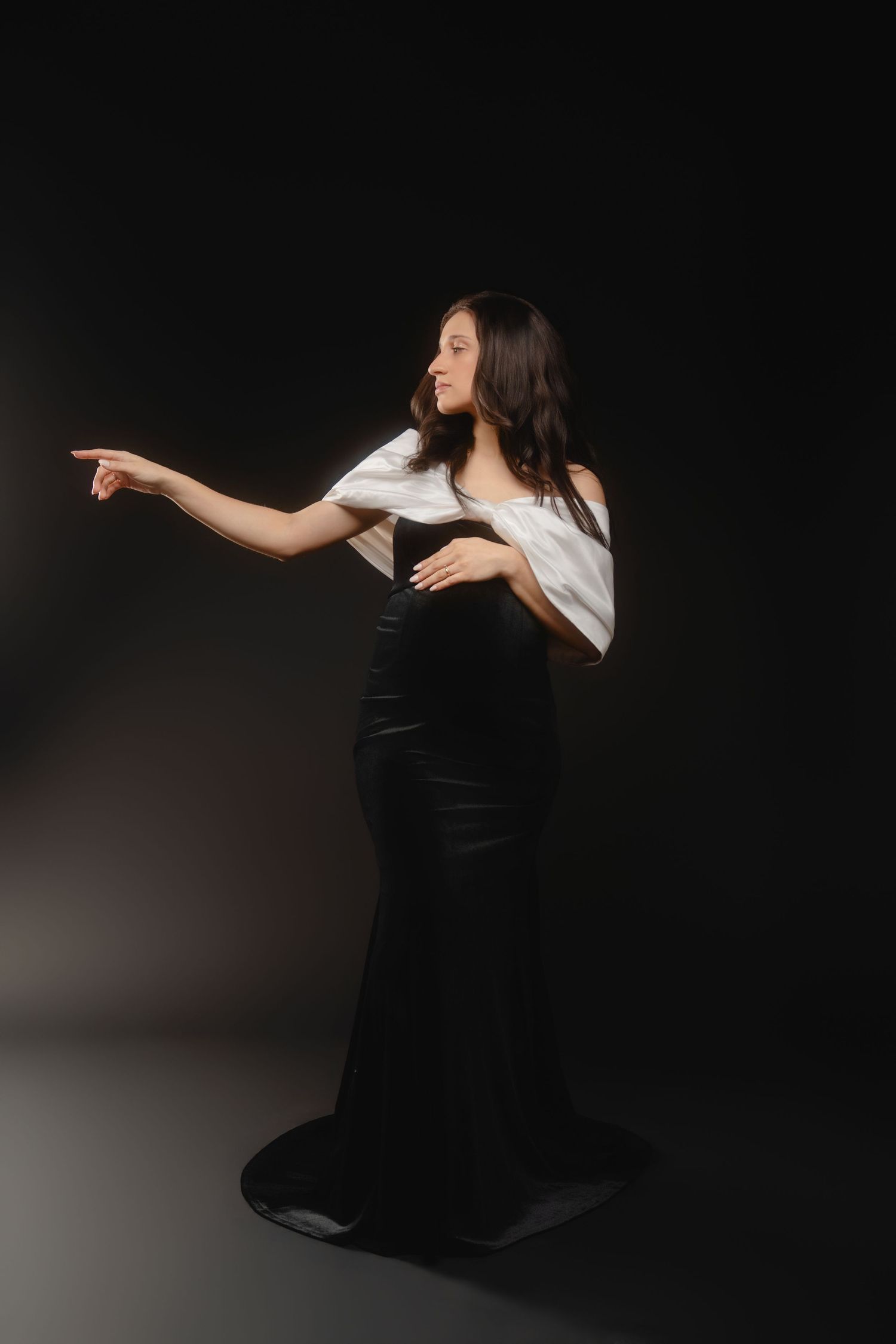 A dramatic black and white portrait shows a woman in dark clothing making expressive dance movements.