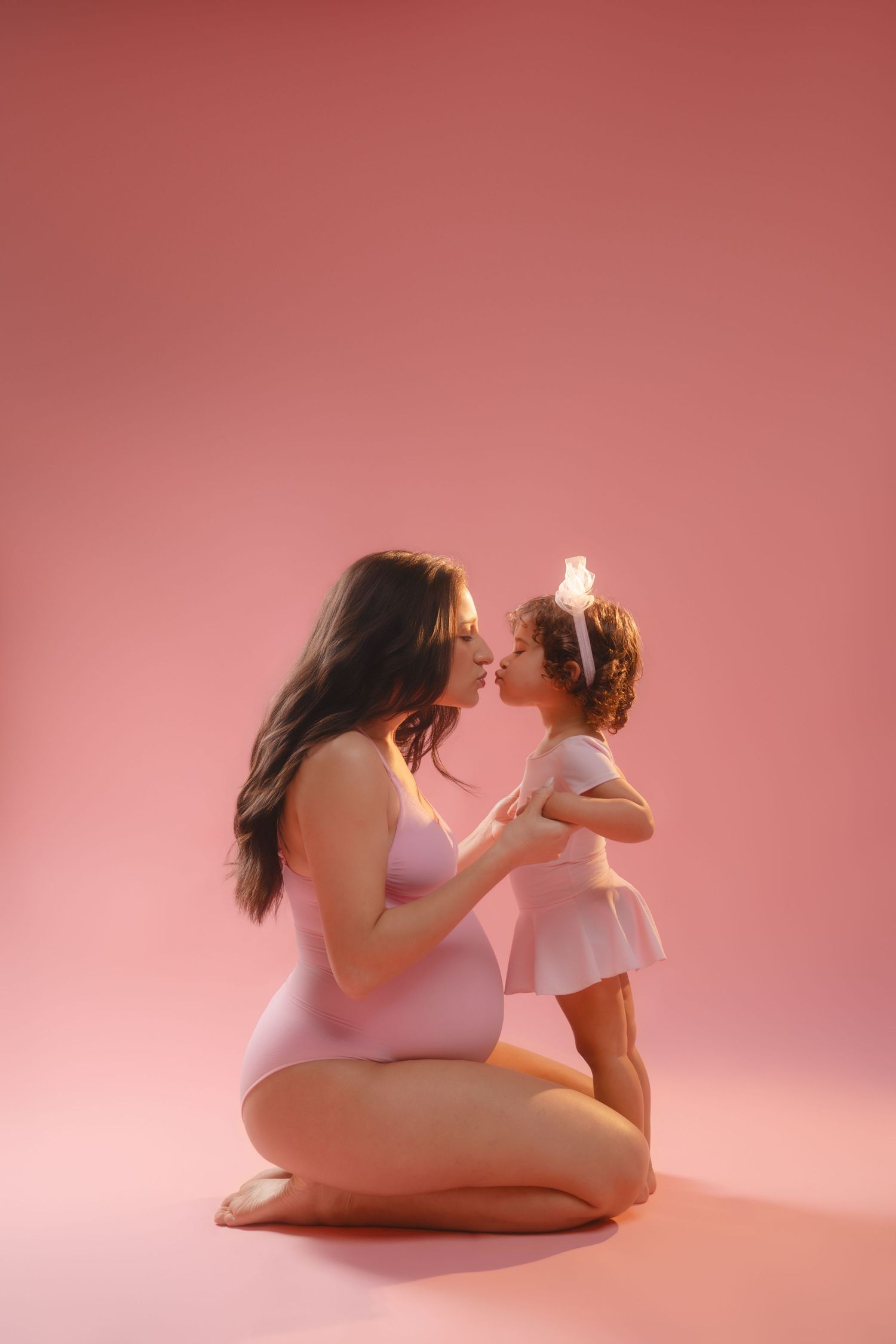 Mother and child share loving moments in pink studio setting during maternity session.
