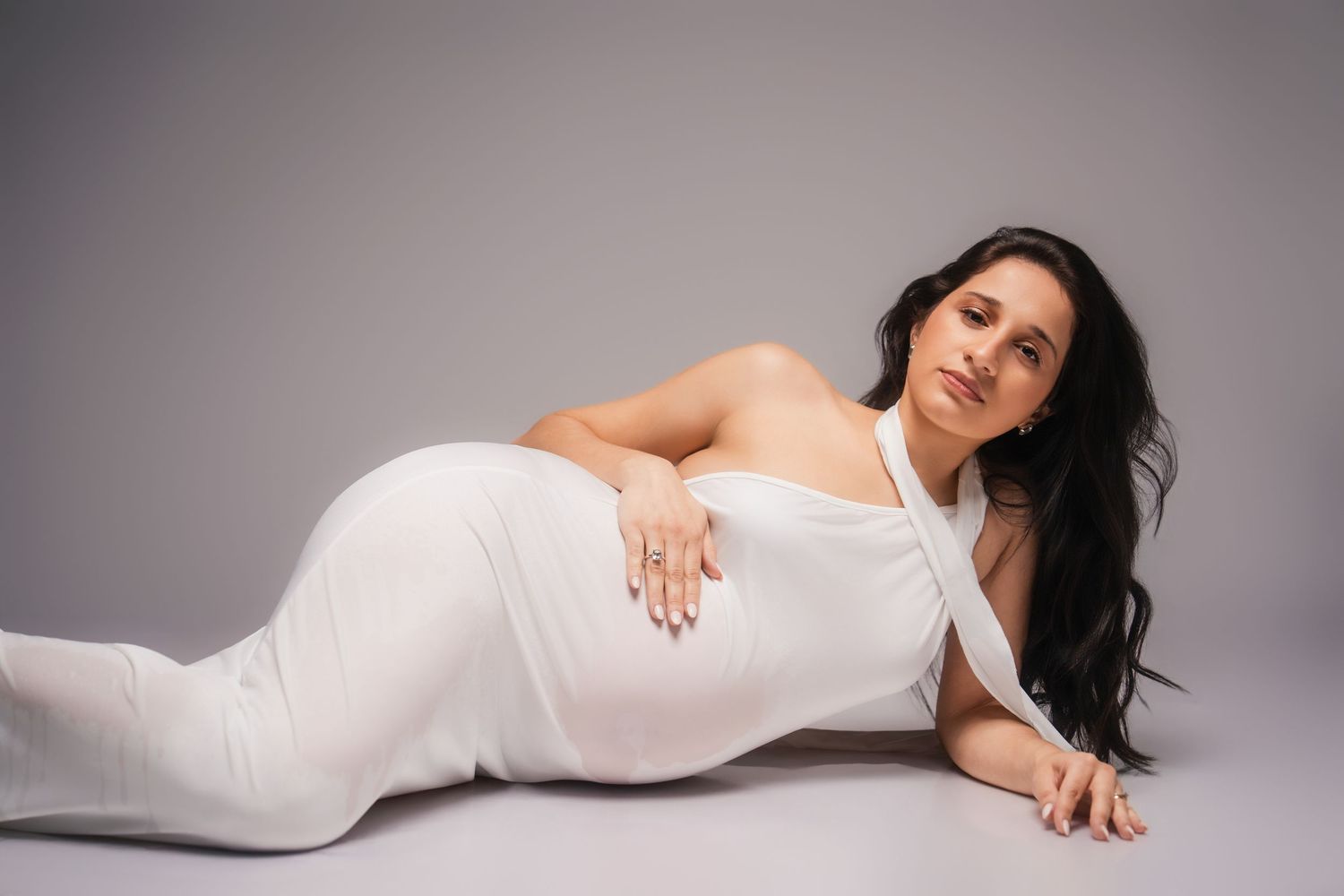 Woman in white dress poses gracefully in a series of artistic maternity portraits against a neutral background.