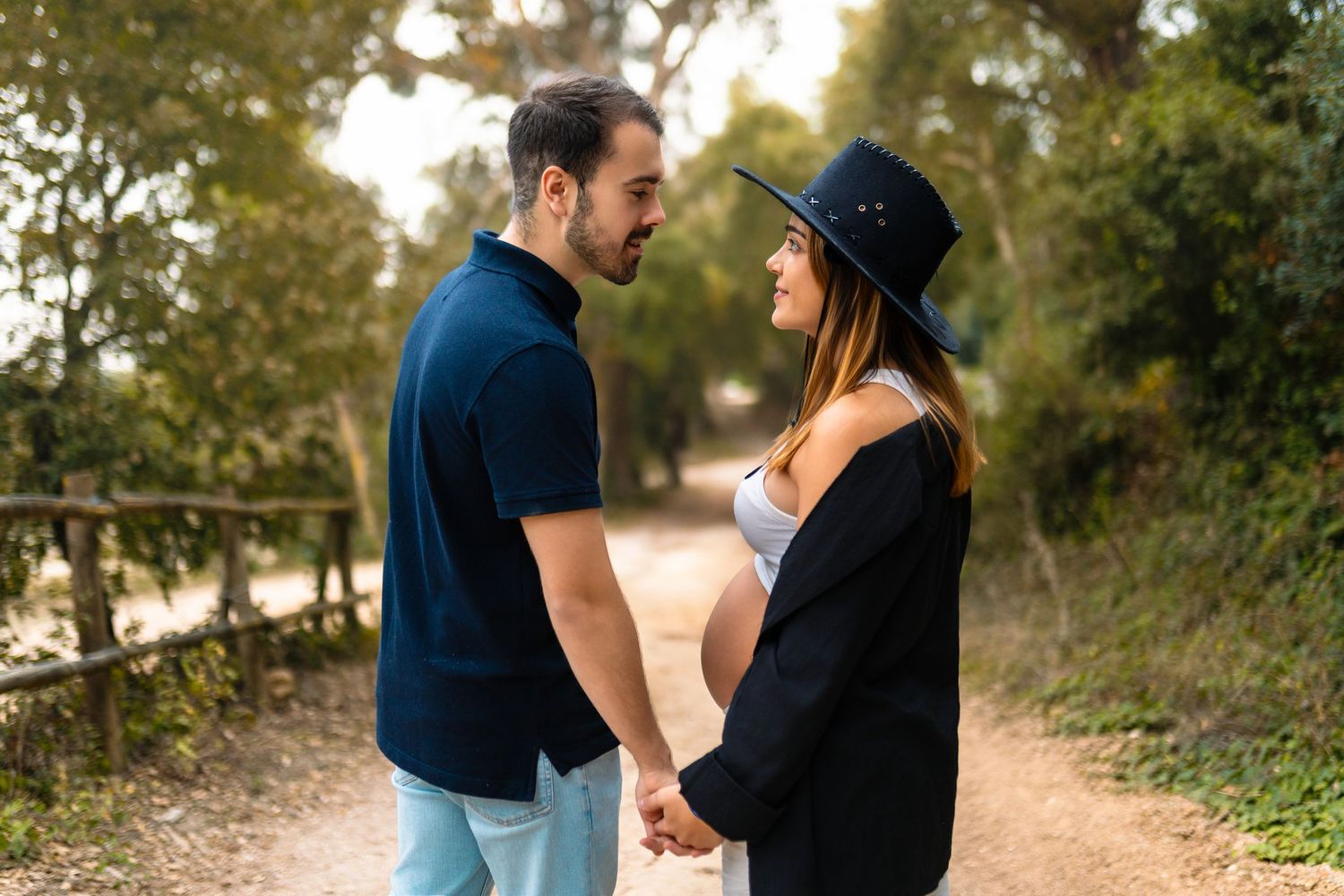 Um casal com mulher grávida, partilha momentos íntimos durante sessão de fotos ao pôr do sol num ambiente arborizado ao ar livre.