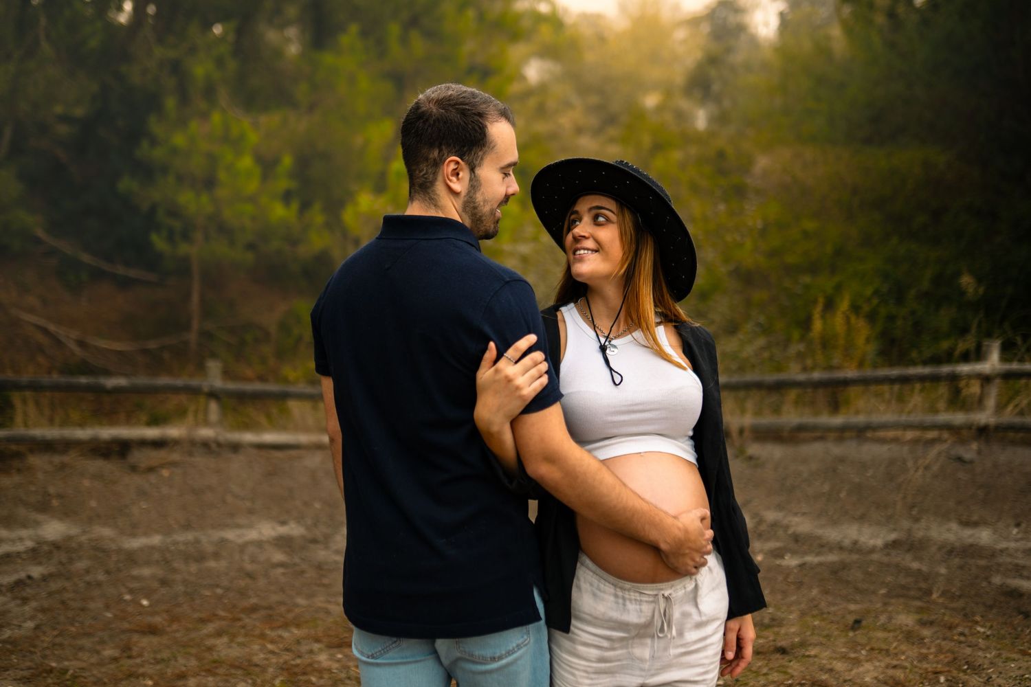 Imagem românticas de  um casal com uma grávida ao ar livre, mostra momentos íntimos num cenário natural ao pôr do sol, n
no campo.