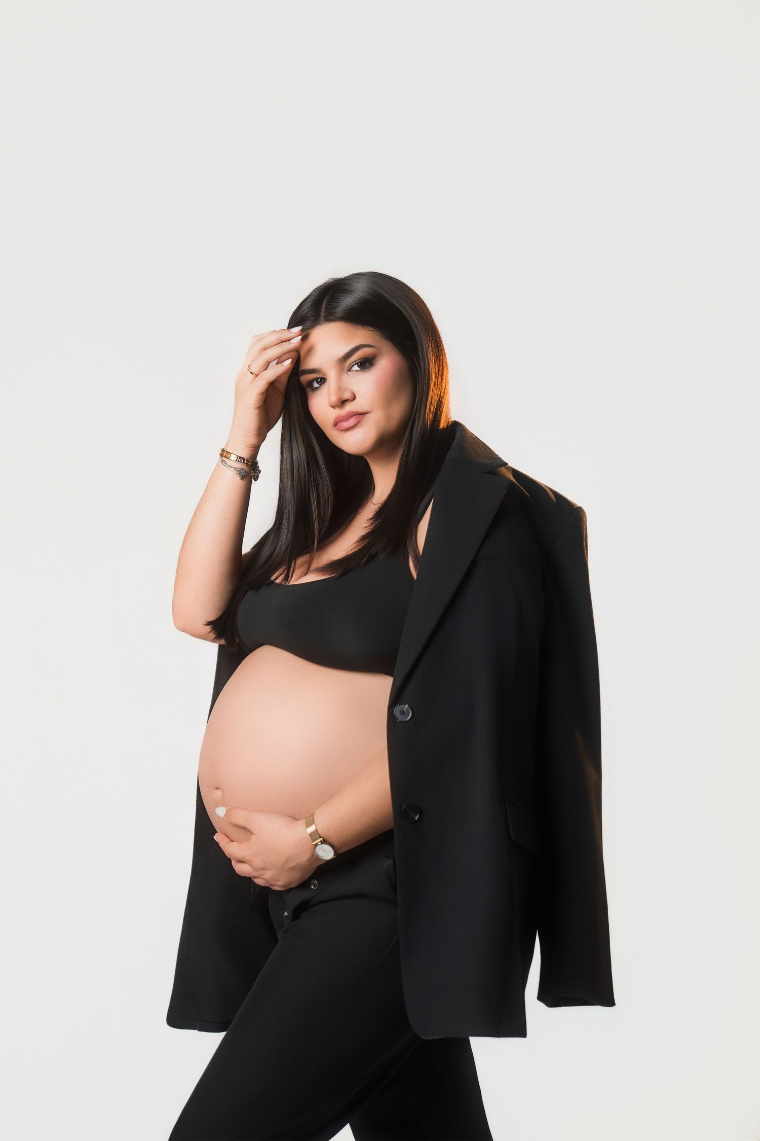 Maternity photoshoot featuring elegant black dress and jacket against white background.