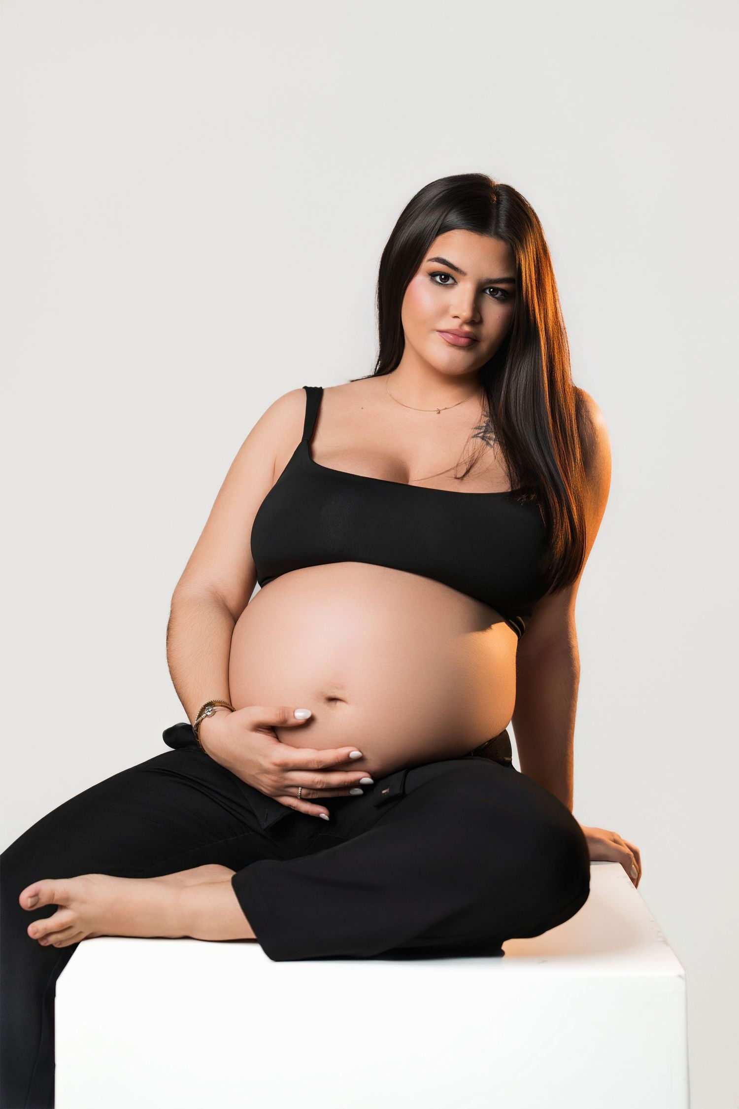 Artistic maternity portrait with woman in black dress posing on white platform.