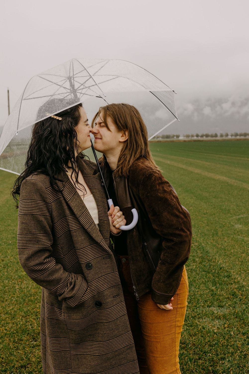 Couple shares intimate moment under umbrella in green countryside.