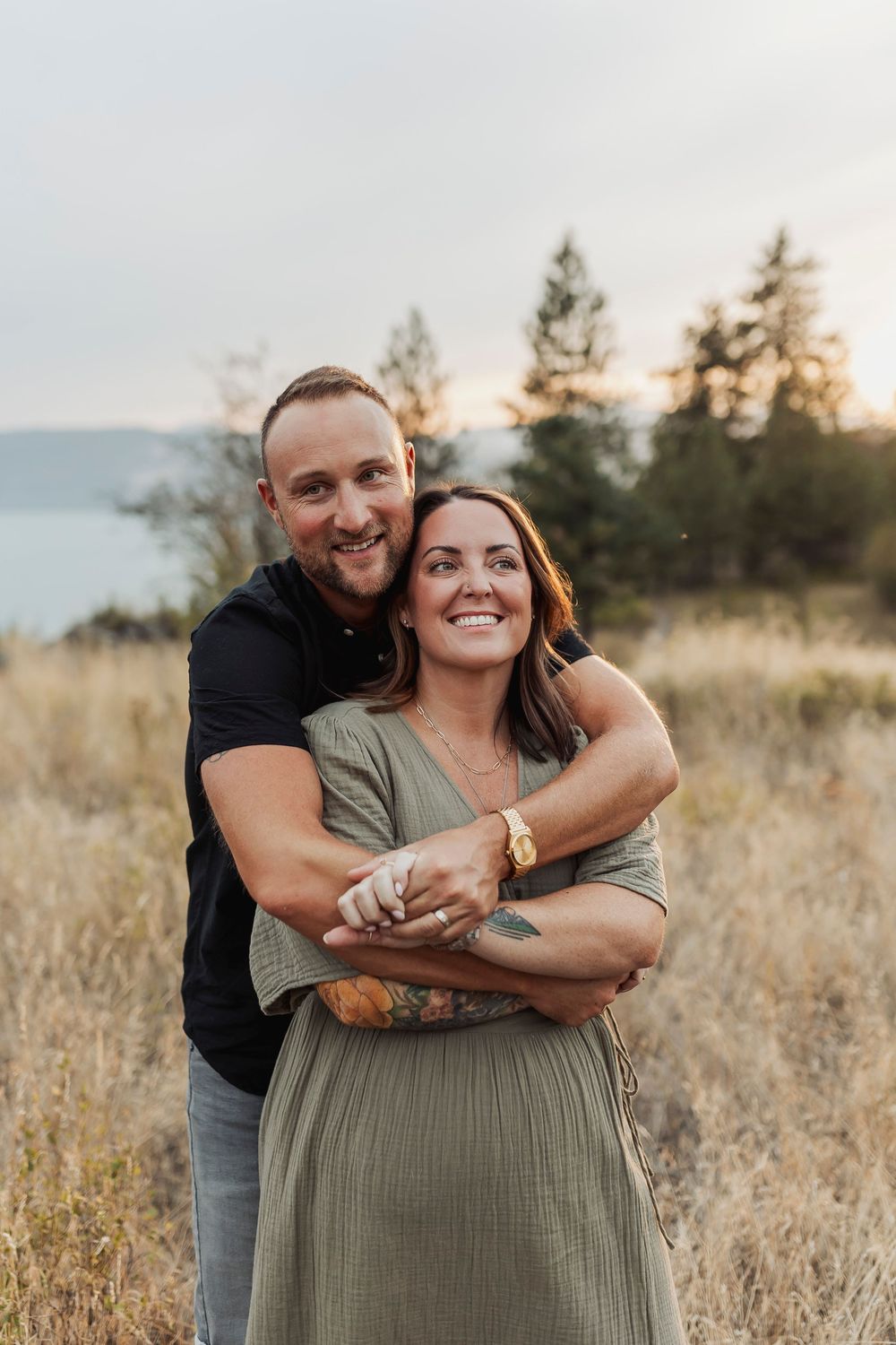 Happy couple embracing in a field with mountain views and golden sunset light.
