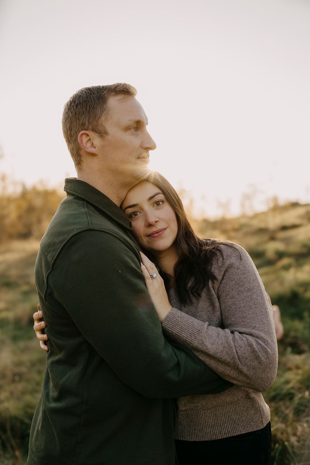 Romantic couple embracing in warm sweaters during golden hour on a hillside.