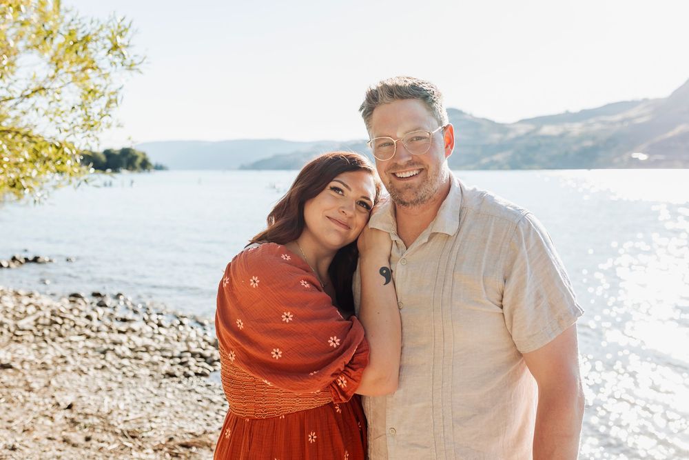 Romantic couple poses by waterfront with scenic mountain views.