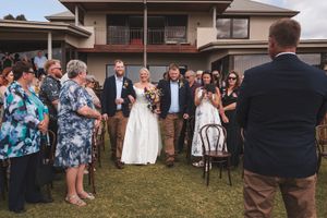 Wedding guests mingle on the lawn outside a brown building.