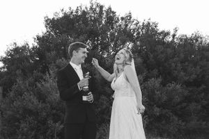Romantic wedding couple embraces under lush trees in an outdoor garden setting at sunset.