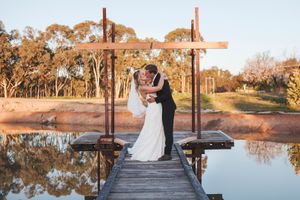 Wedding couple poses on wooden boardwalk near tranquil lake during golden hour.