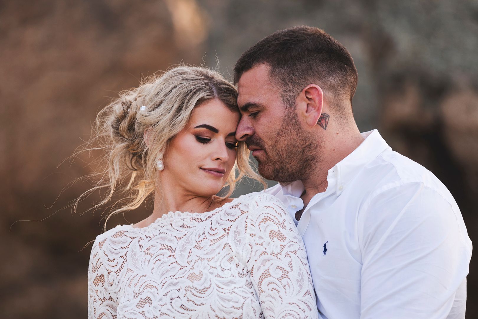 Romantic couple embraces against rocky landscape during golden hour sunset photo session.