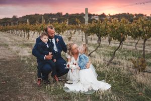 Wedding couple poses in vineyard during stunning pink and purple sunset.