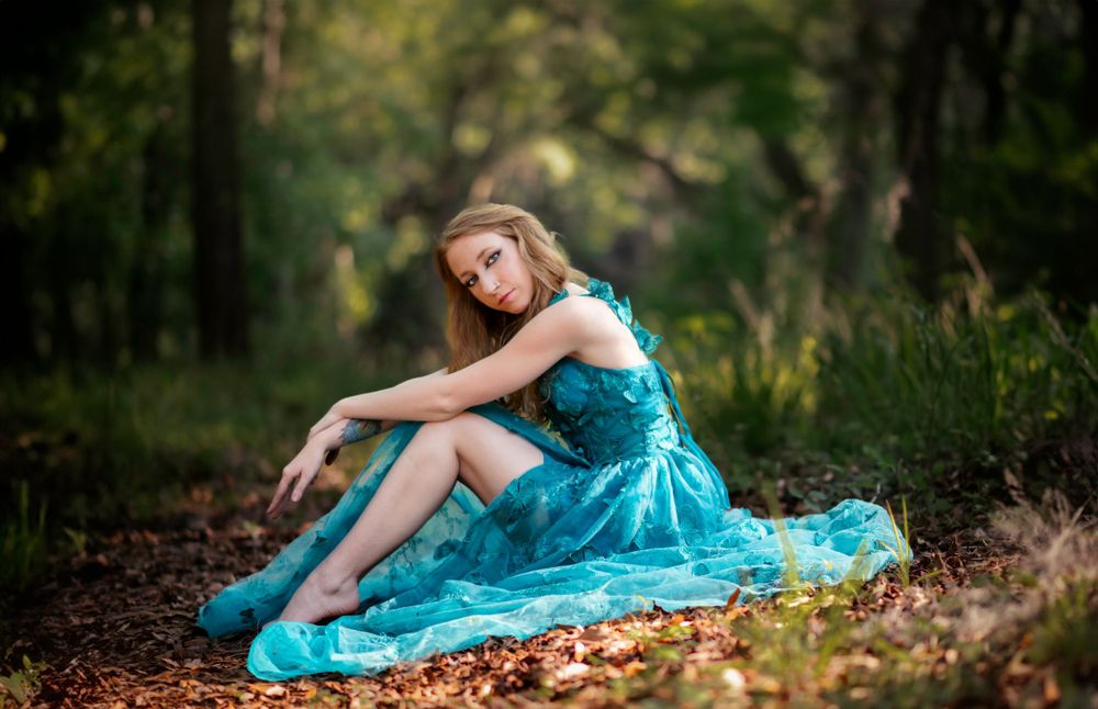 Artistic portrait featuring flowing blue dress against autumn forest floor.