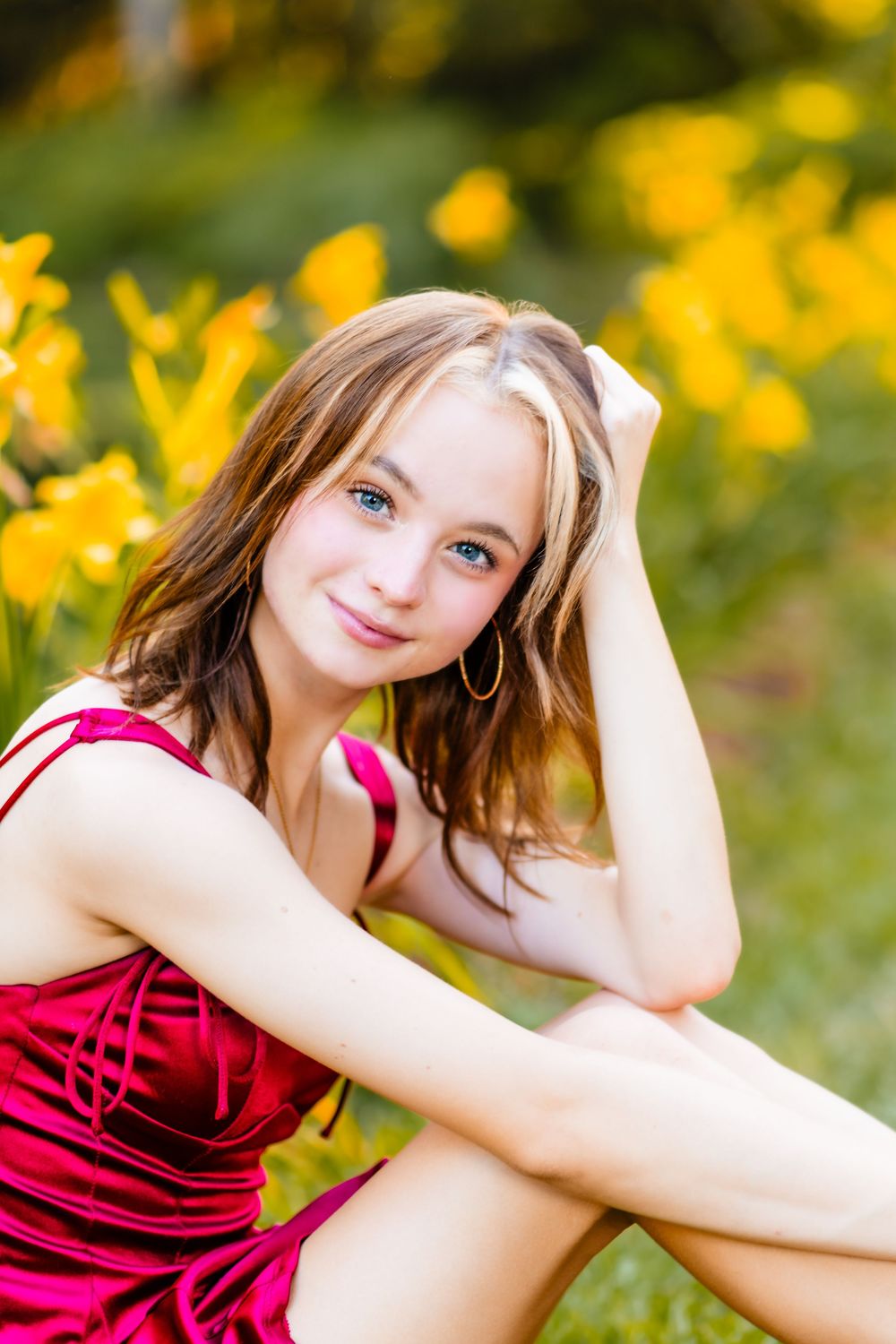 A thoughtful pose outdoors in a red dress with vibrant yellow flowers and greenery in the background.