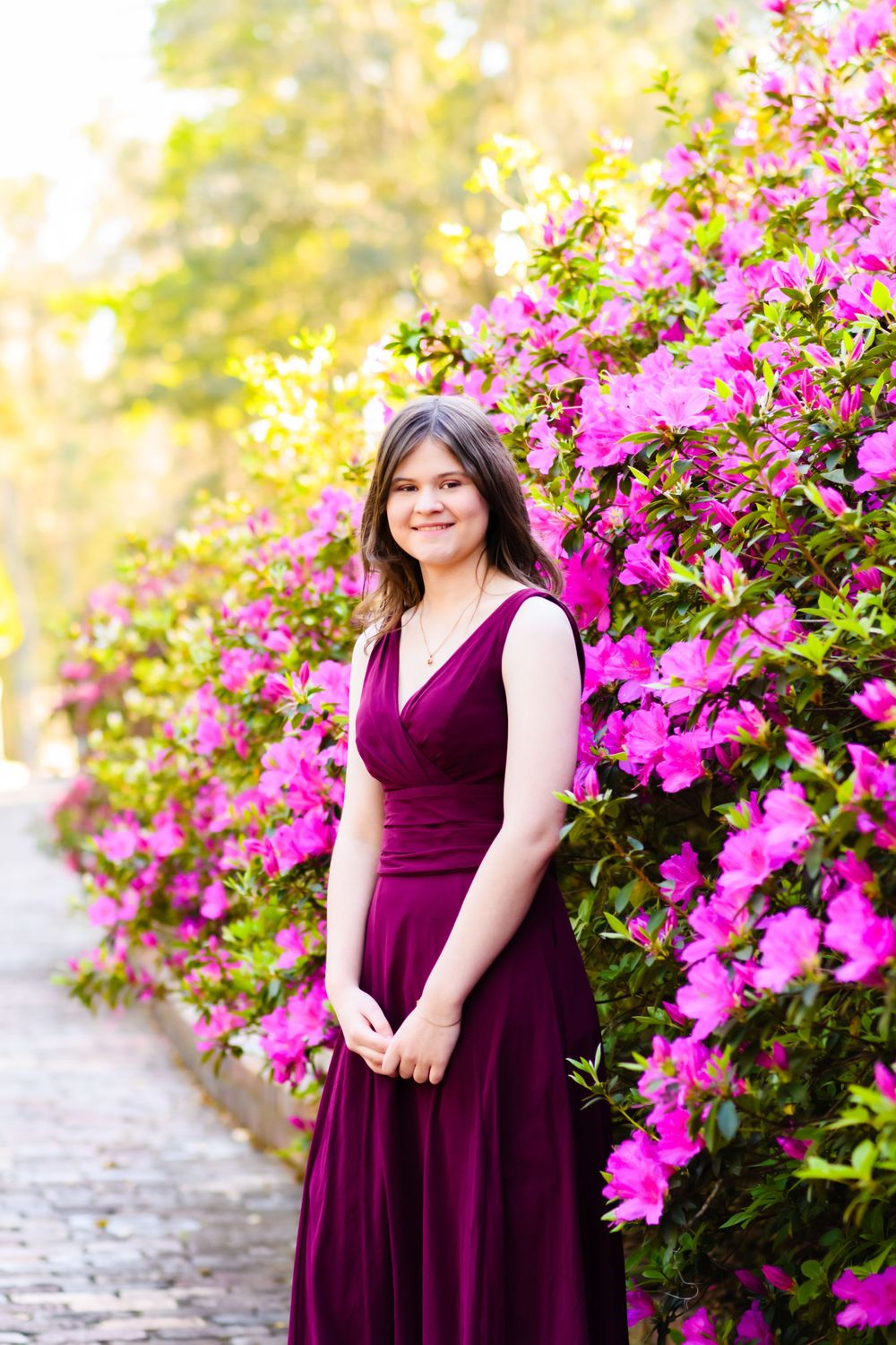 Someone in an elegant burgundy gown stands by vibrant pink bougainvillea flowers in a garden setting.