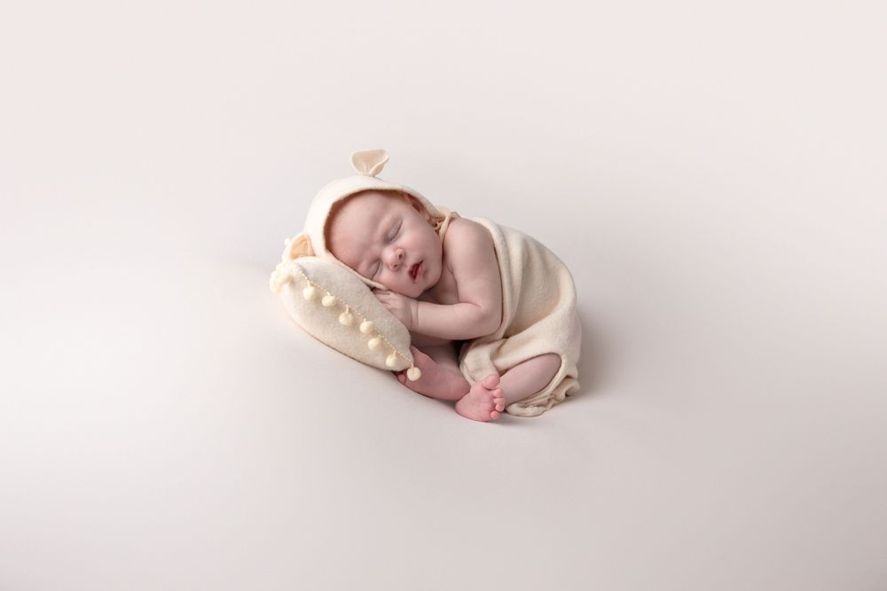 Sleeping newborn baby in cream bunny outfit and bonnet resting on a star-shaped pillow on white background.