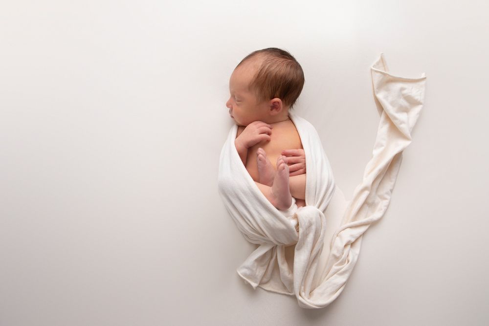 Peaceful newborn baby wrapped in white fabric lying on a white background in a professional studio photo.