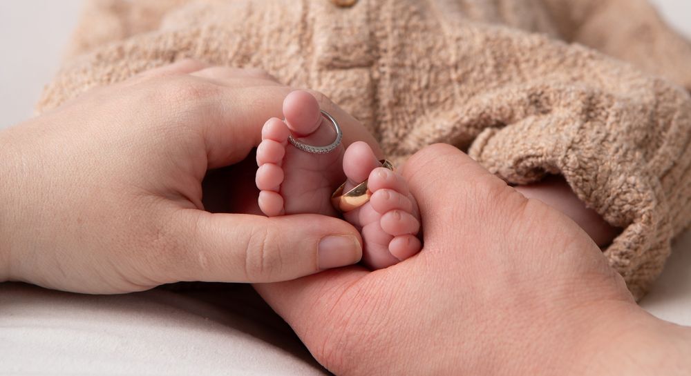 Close-up of tiny newborn baby feet being gently held by parent hands in a studio photo.