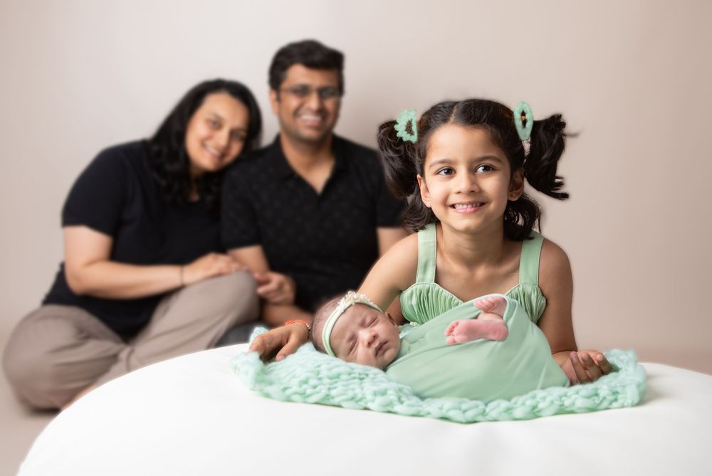 Family portrait with parents, toddler girl, and newborn baby wrapped in mint green on a white surface.