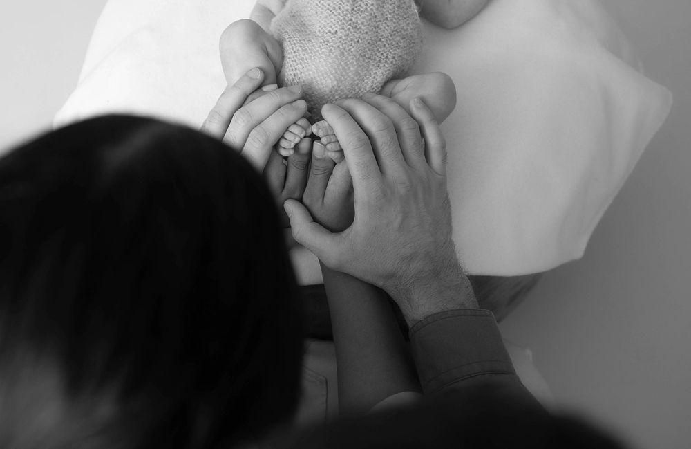 Parents tenderly cradle their newborn baby's tiny feet together in a black and white photo.