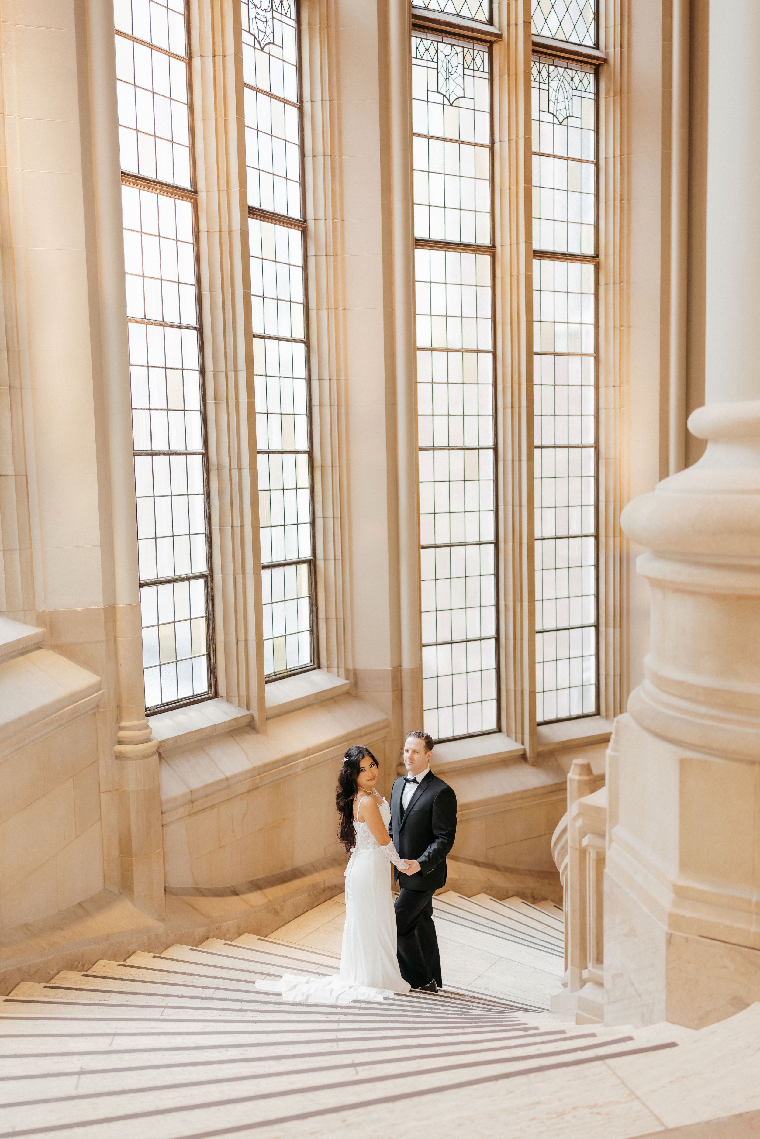 Bride and groom share an intimate moment in an elegant corridor with tall leaded glass windows.