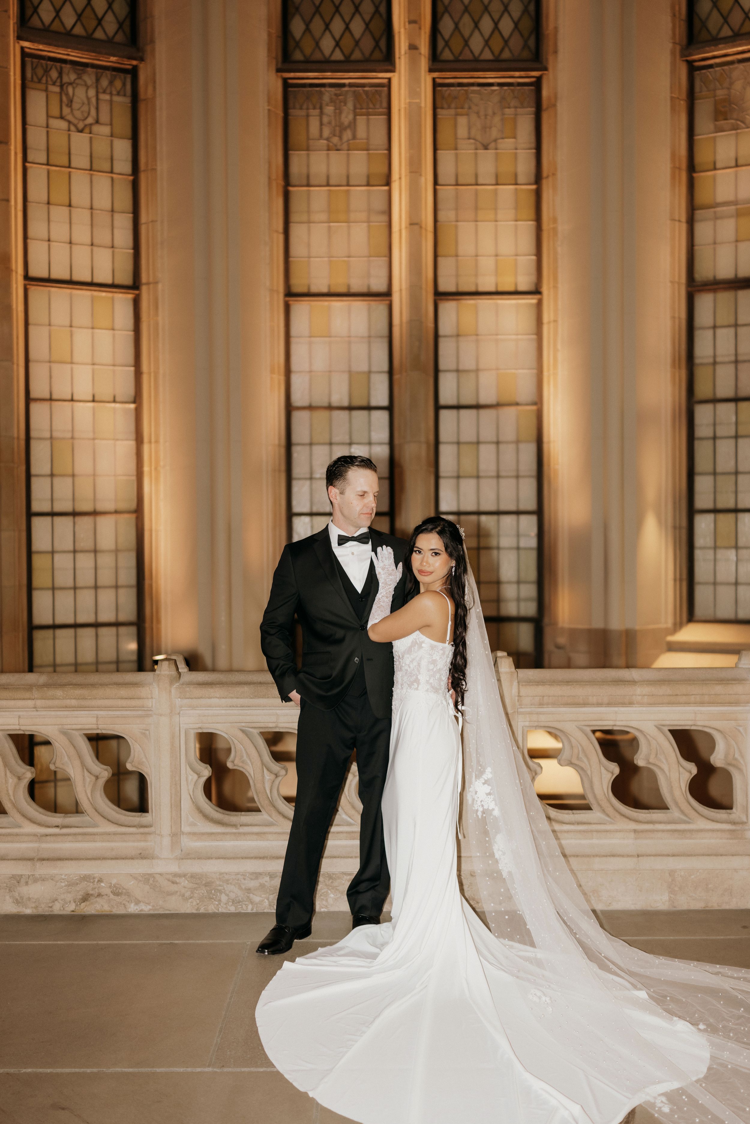 Newlyweds share an intimate moment in front of ornate Gothic windows with the bride's long train flowing behind.